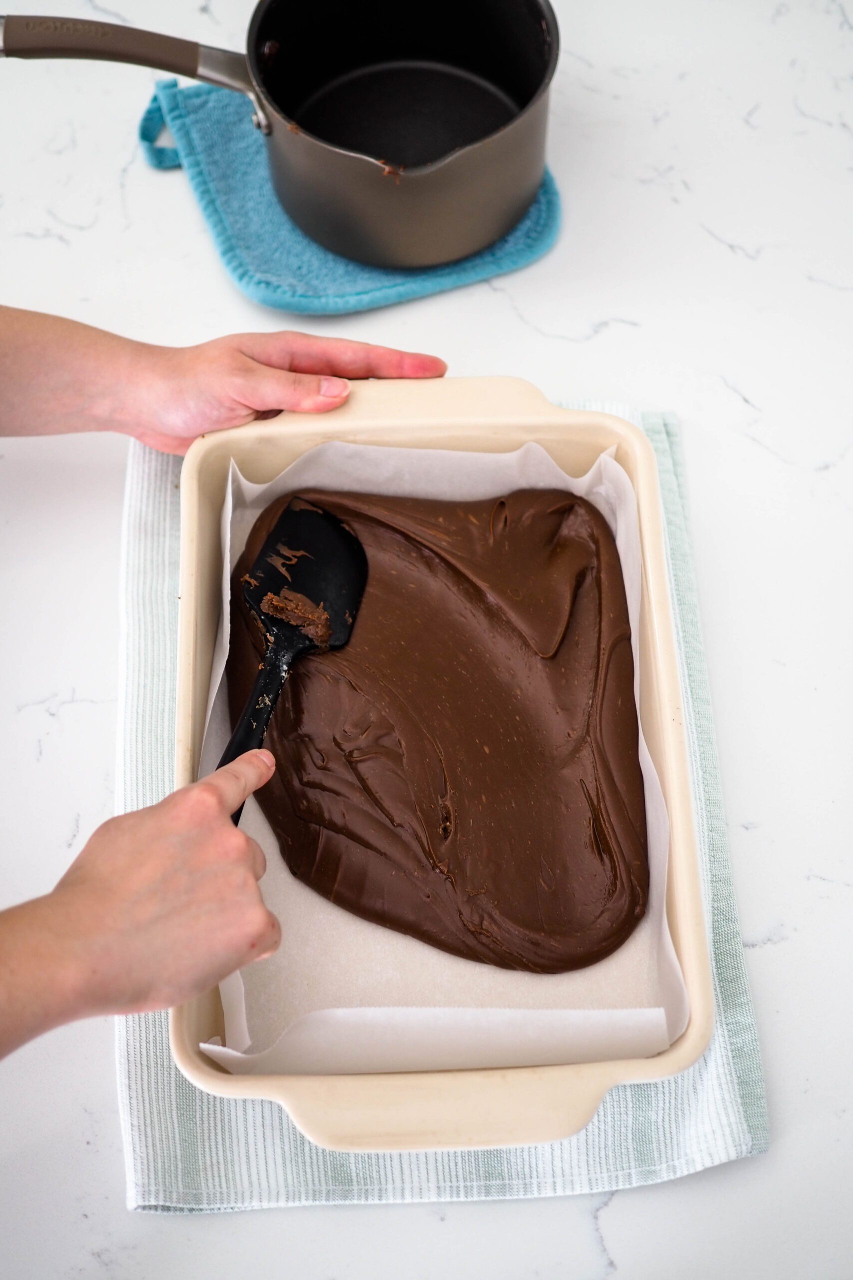 A spatula spreads the fudge to the edges of a baking dish.