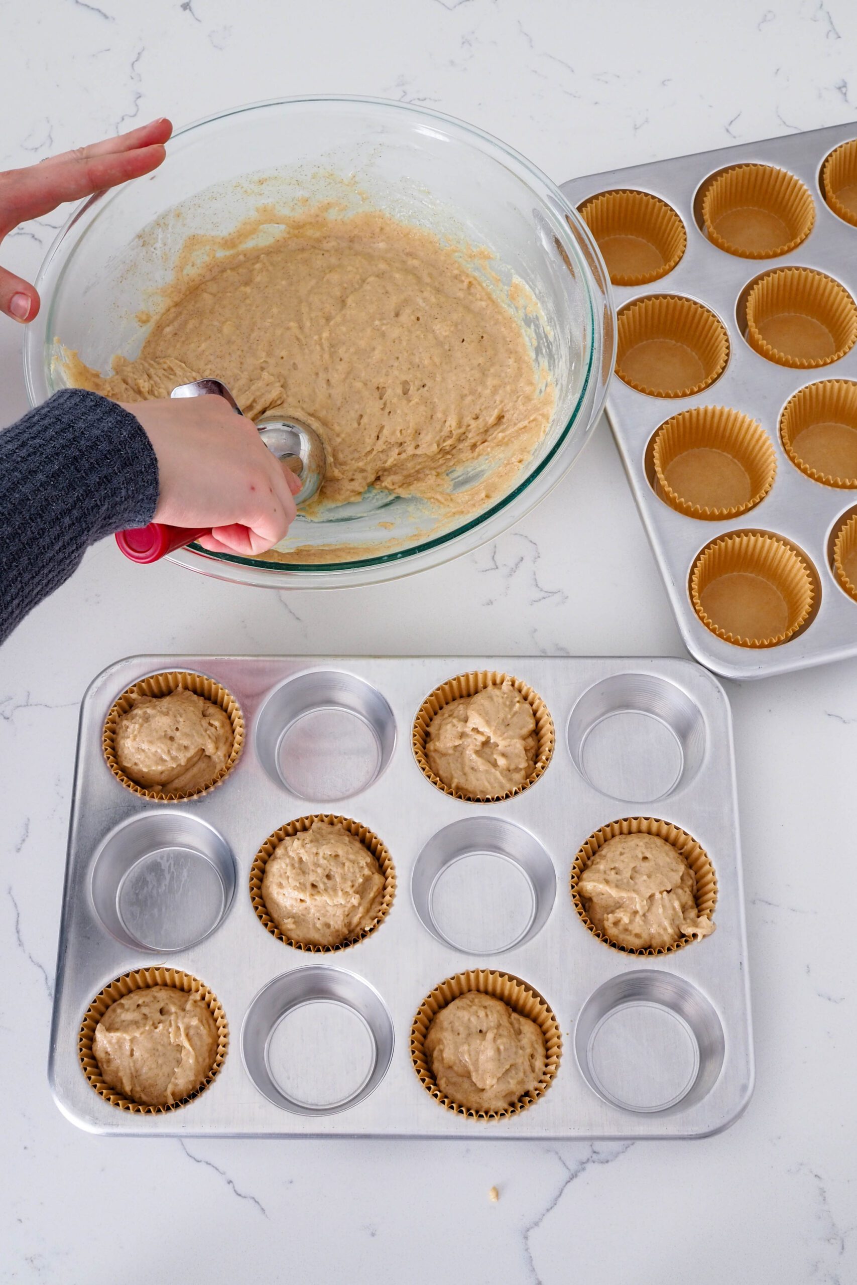 A hand fills muffin cups with caramel chai muffin batter. The muffin pan has every other hole lined.