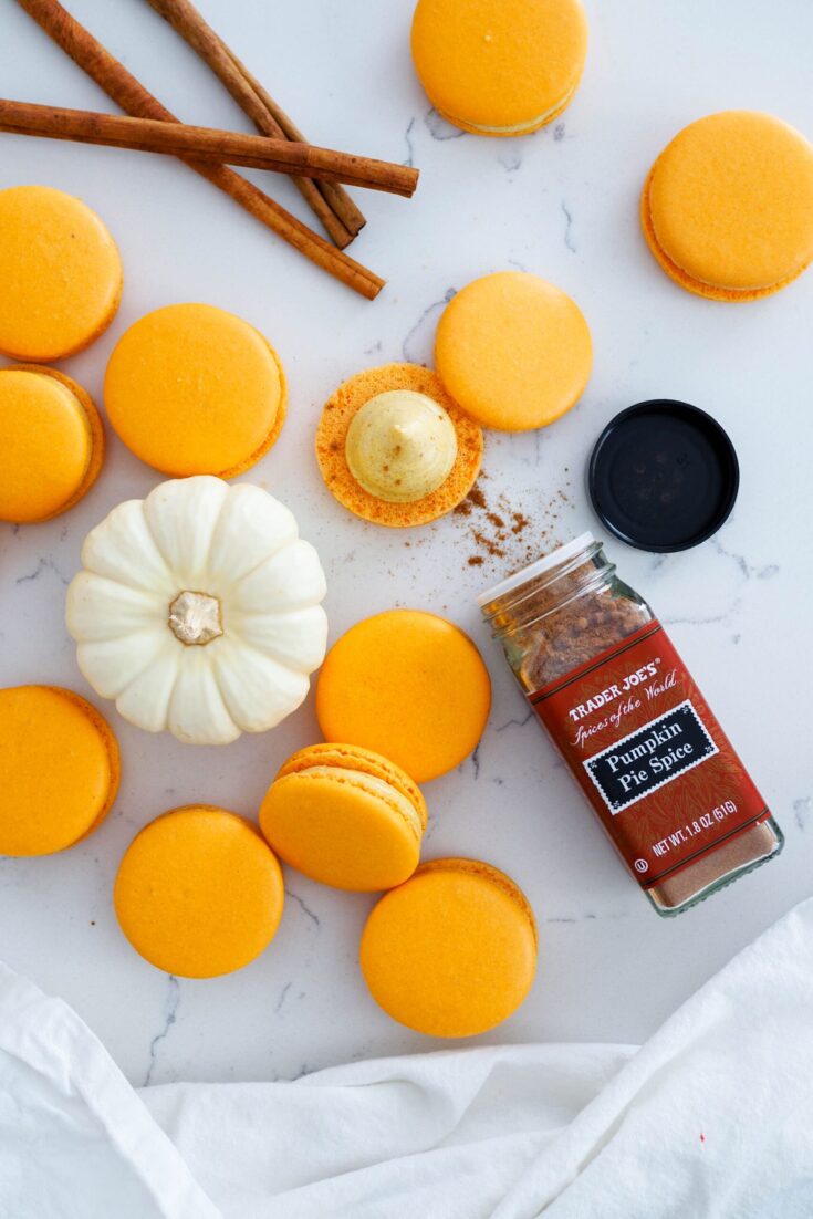 An open jar of pumpkin pie spice next to a stack of macarons and a mini white pumpkin.