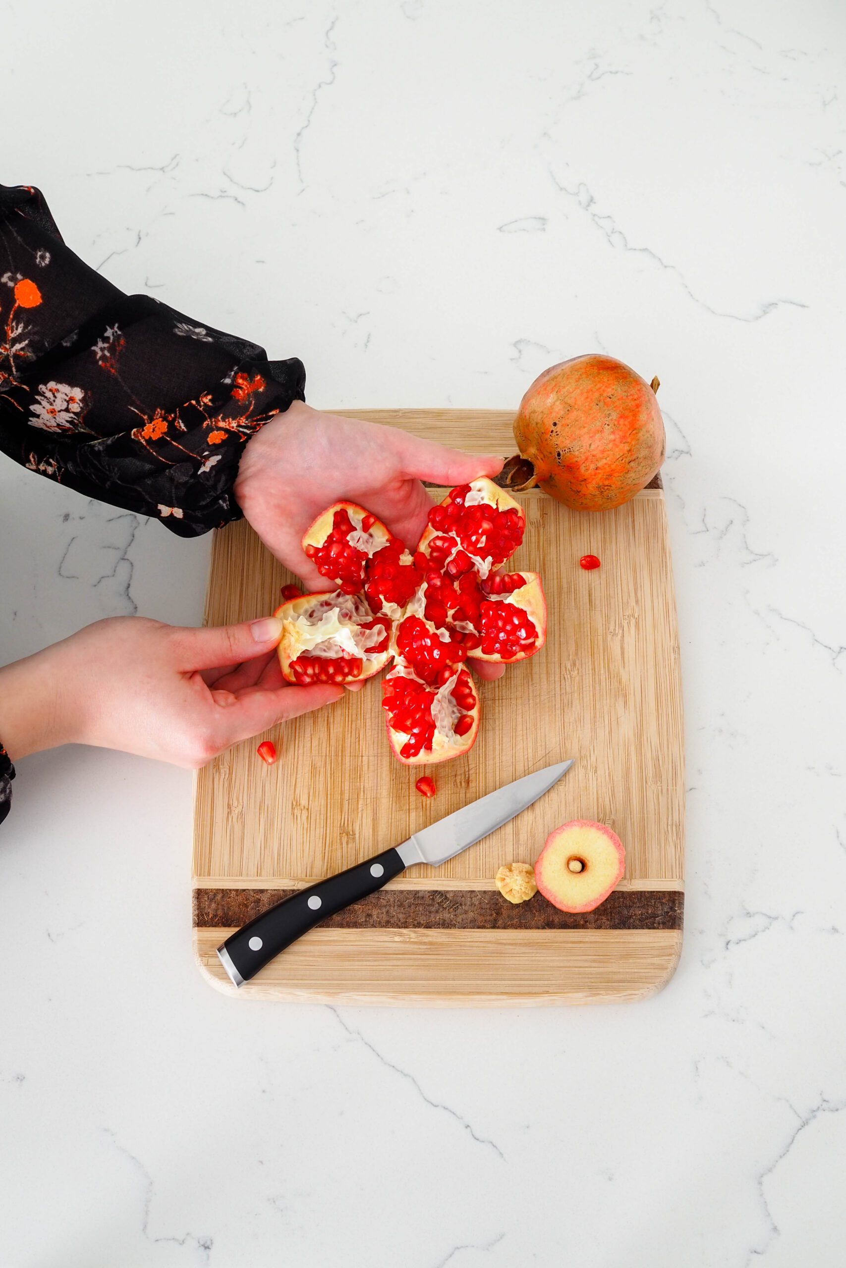A hand pulls a section of pomegranate away from the fruit.