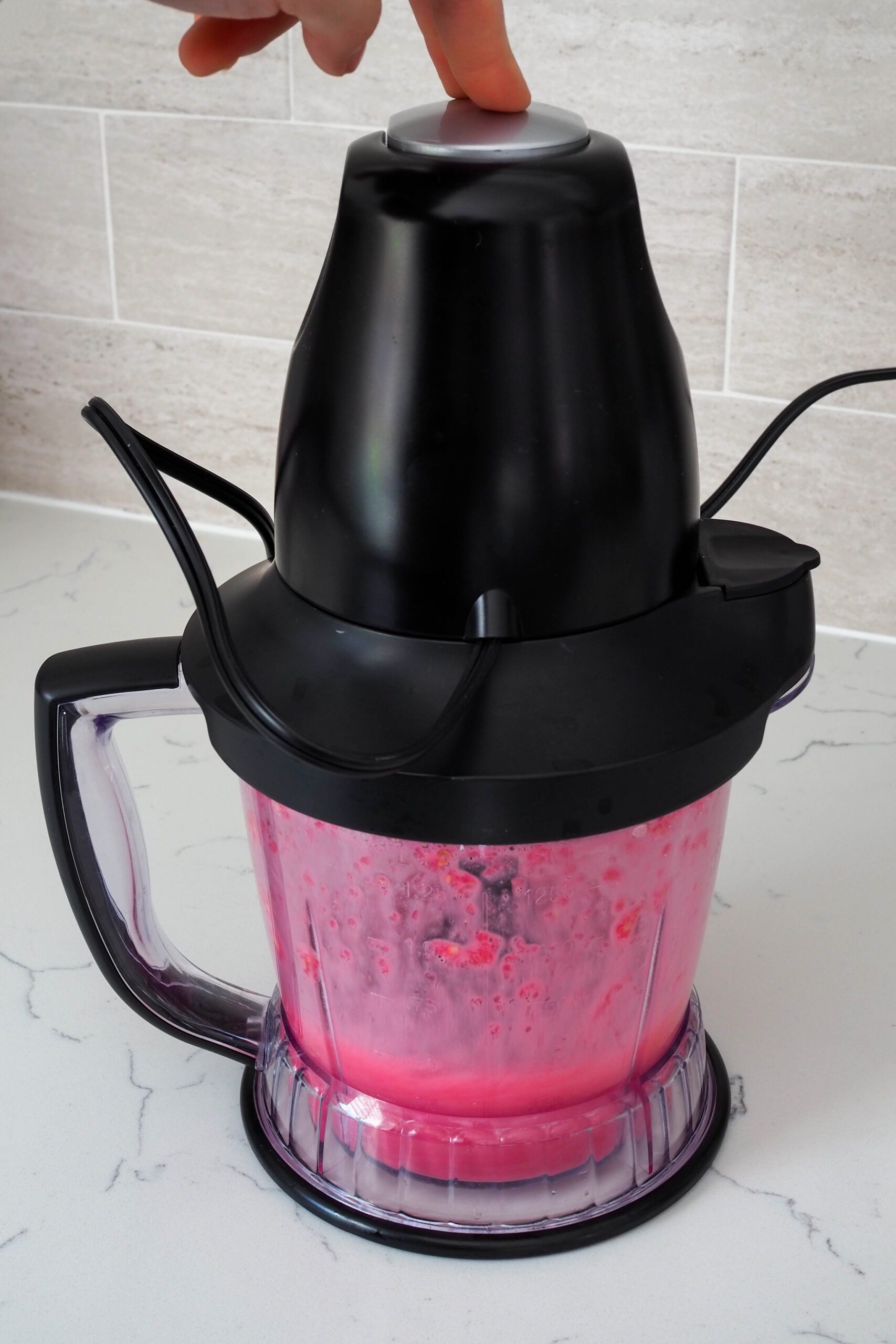 A hand presses down on a blender to blend dark red pomegranate juice.