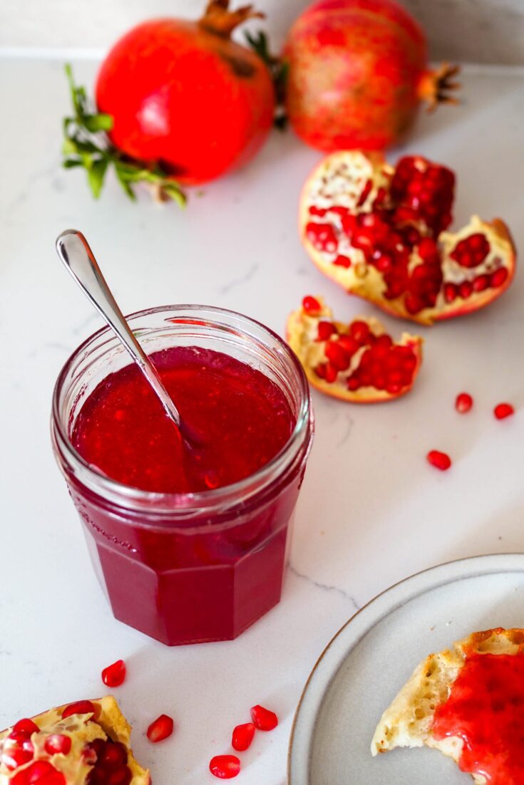 A jar of pomegranate jelly with a spoon sticking out of it.
