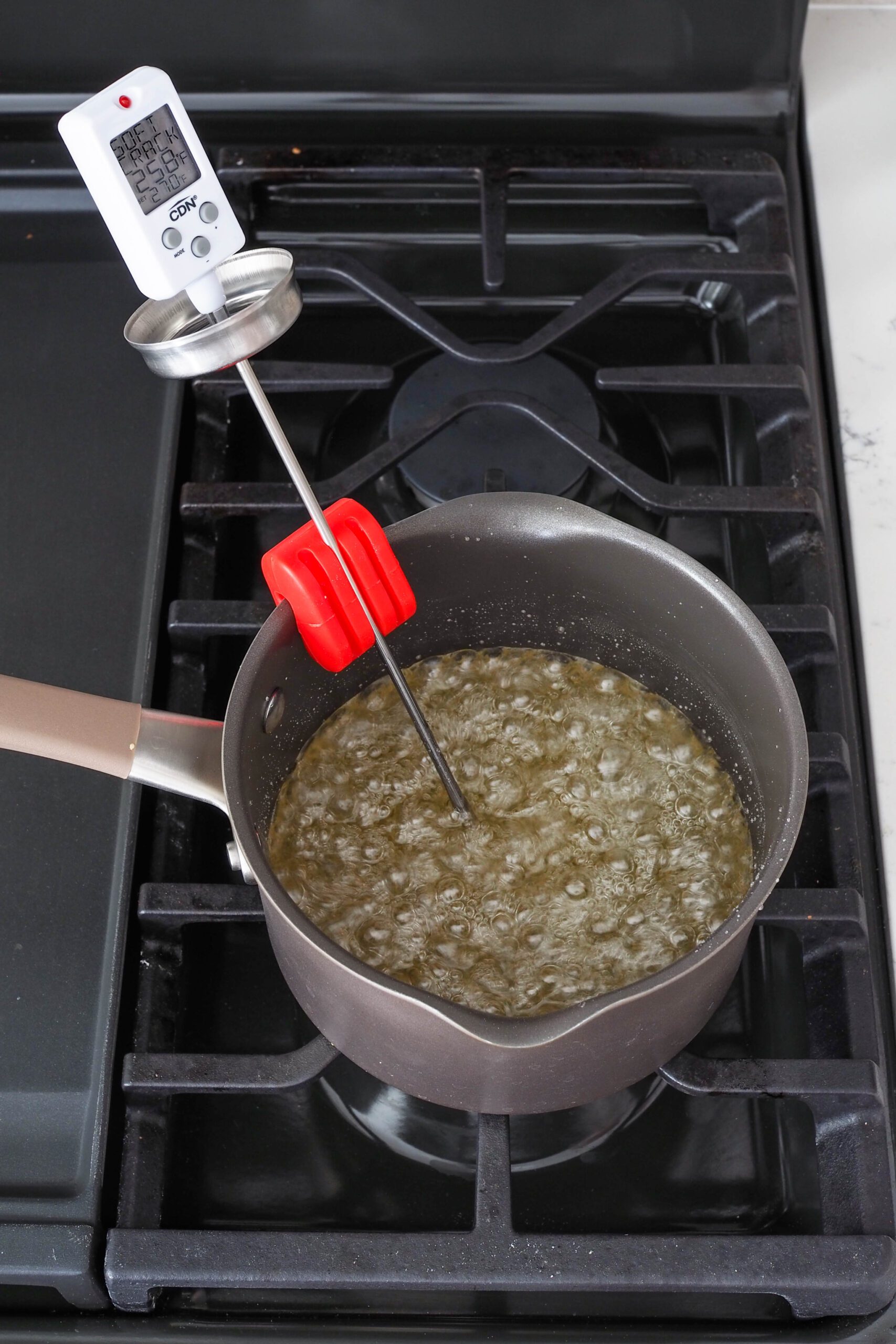 Hot sugar syrup in a pan over a burner with a digital candy thermometer.