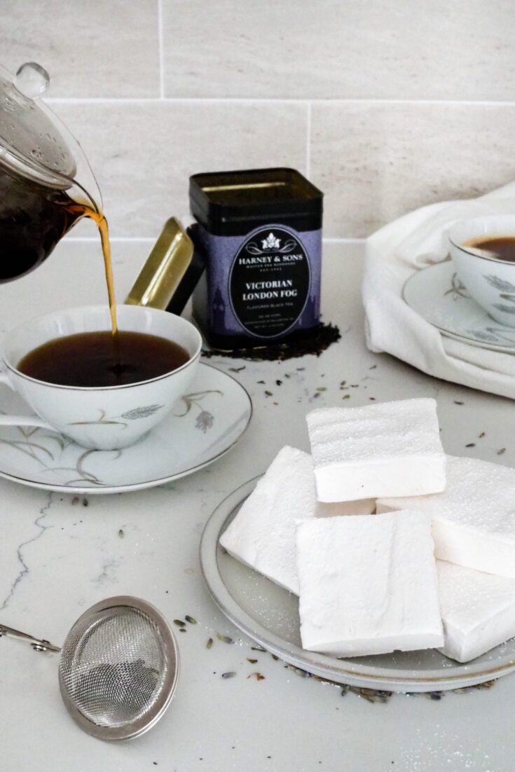 A plate of marshmallows is next to a cup of Earl Grey tea being poured.