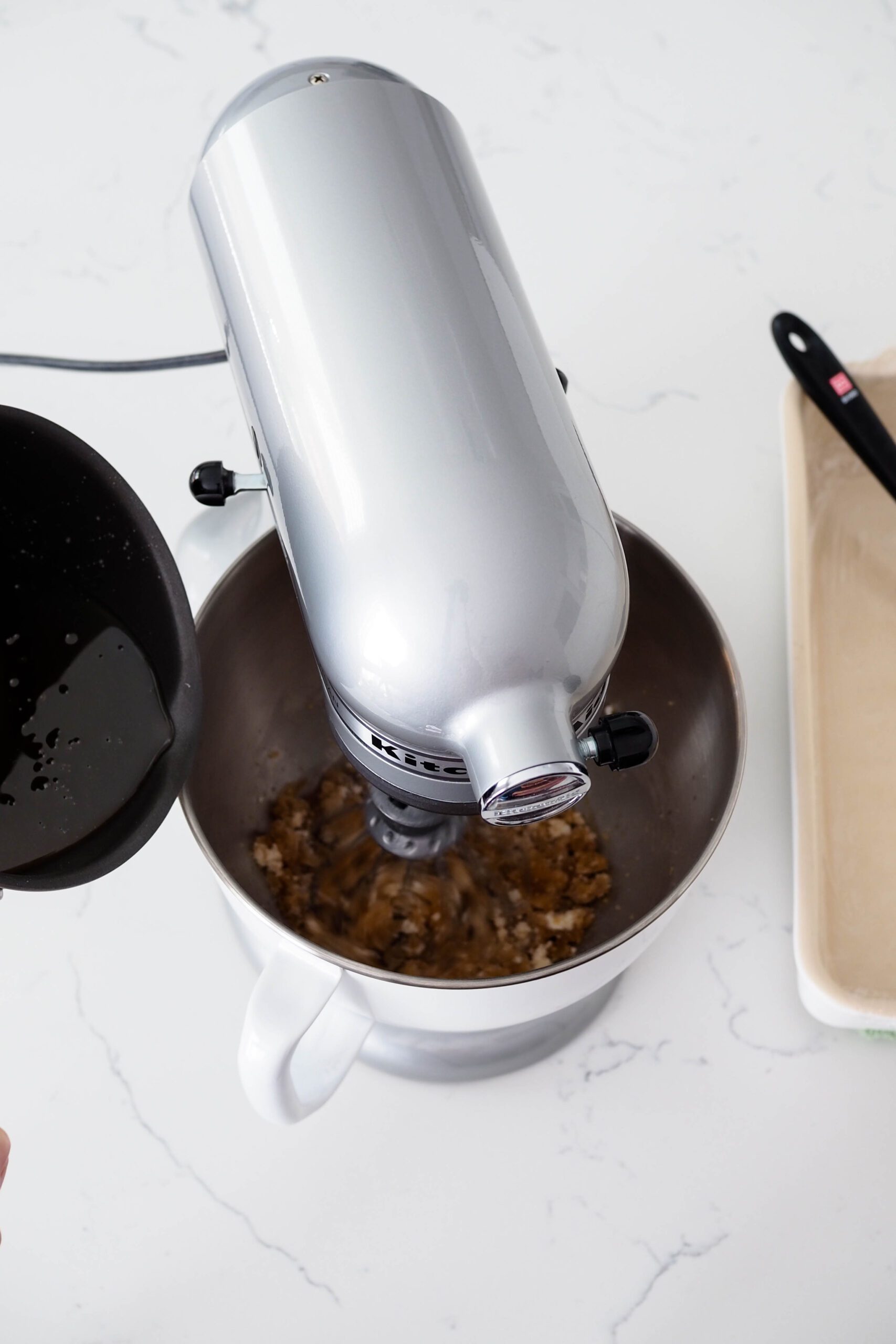 A pan begins to pour syrup into the bowl of a stand mixer.