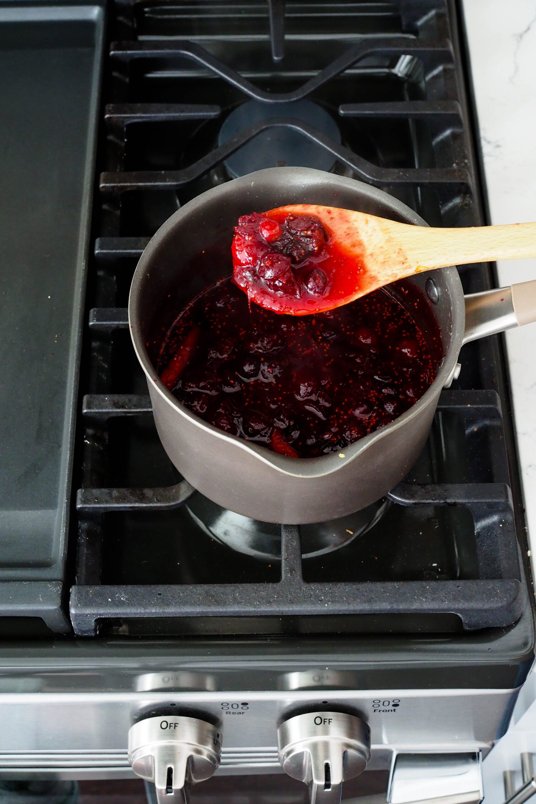 A wooden spoon holds up some cranberry sauce.