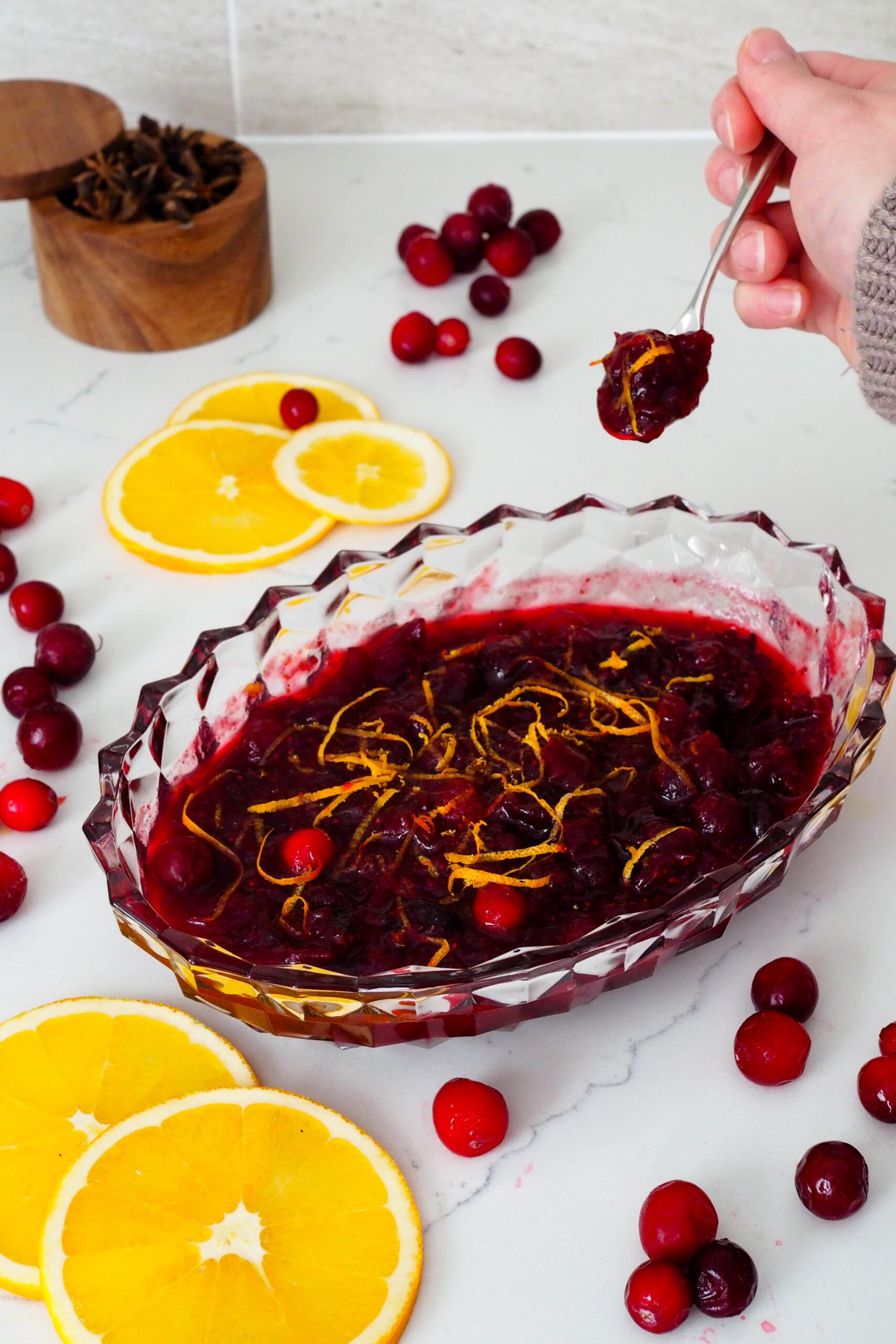 A hand scoops a small serving of cranberry sauce out of a crystal serving dish.