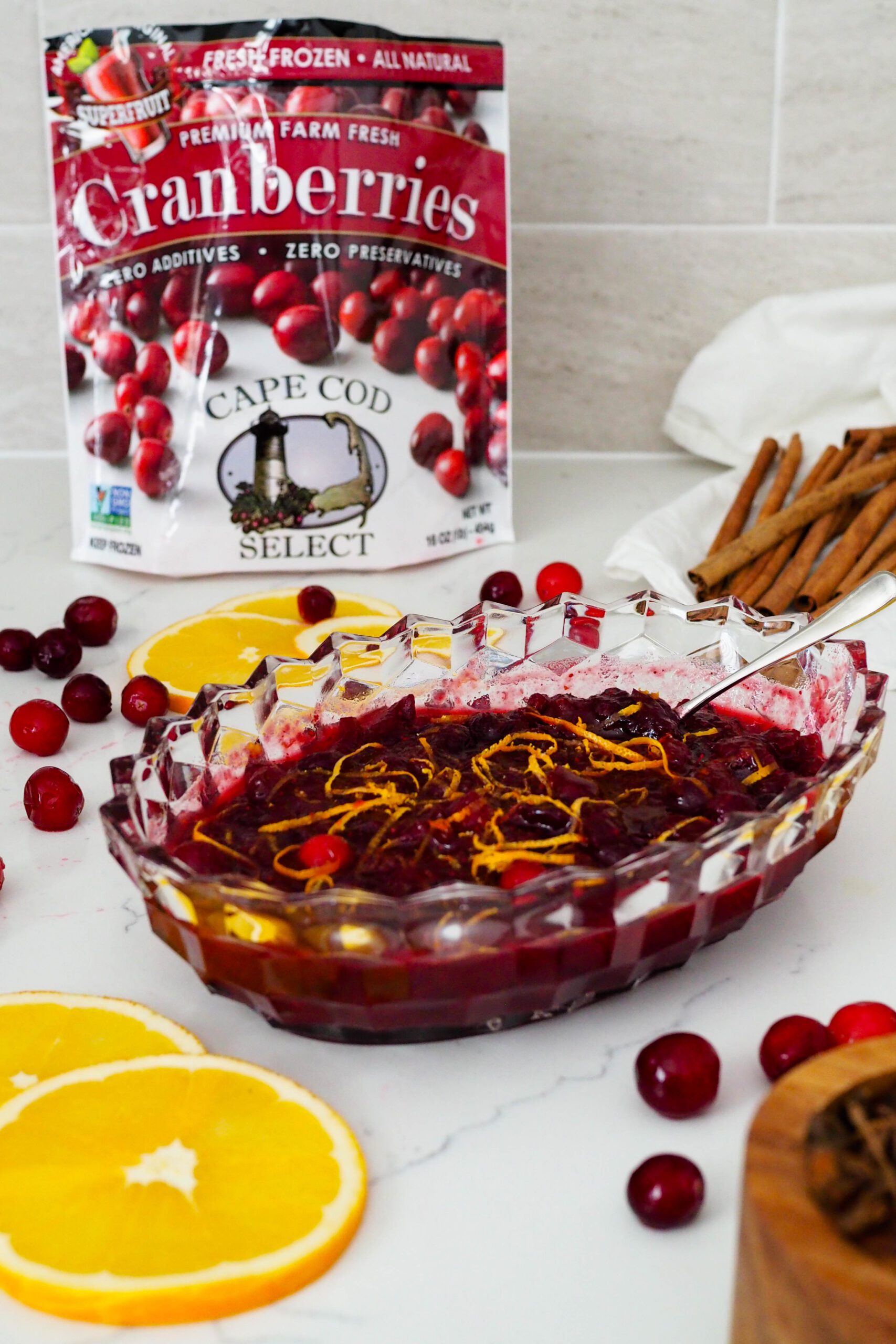 A Cape Cod Select frozen cranberries bag in the background of a crystal dish full of cranberry orange sauce.