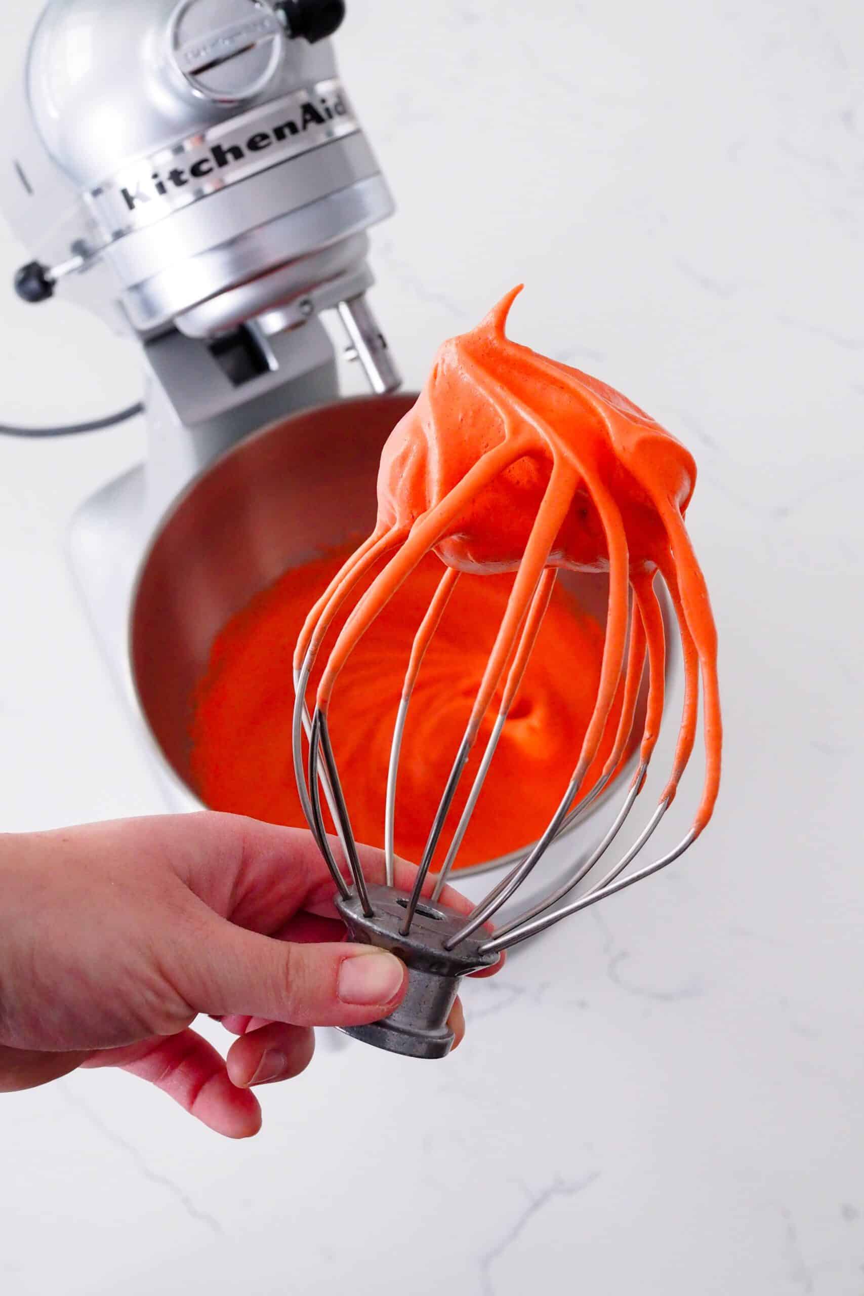 A clump of red meringue with stiff peaks on a KitchenAid whisk attachment.