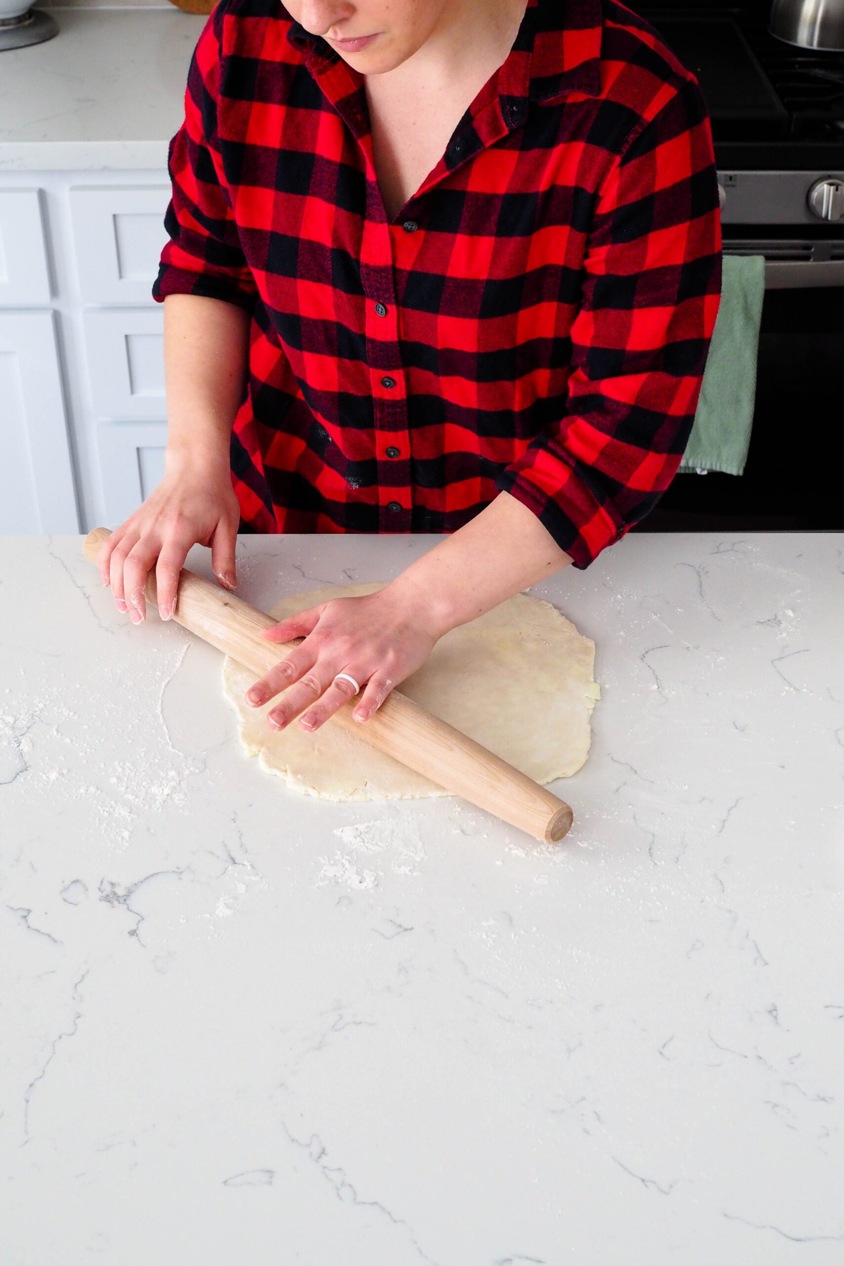 A woman rolls a rolling pin over a round of pie dough.