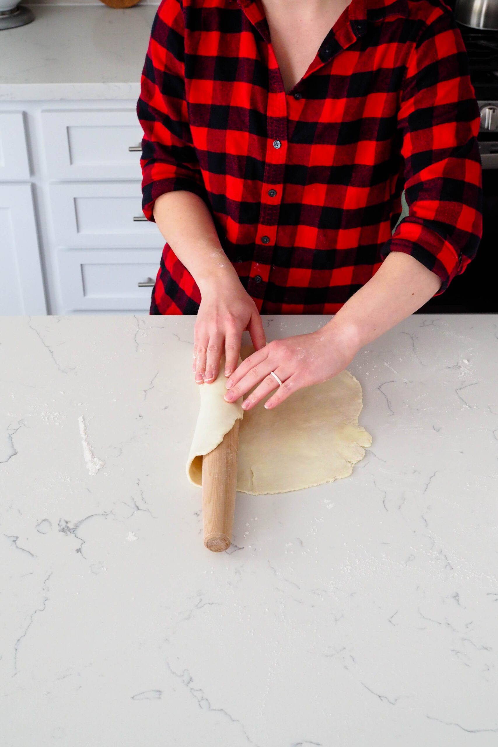 A woman wraps pie dough around a rolling pin.