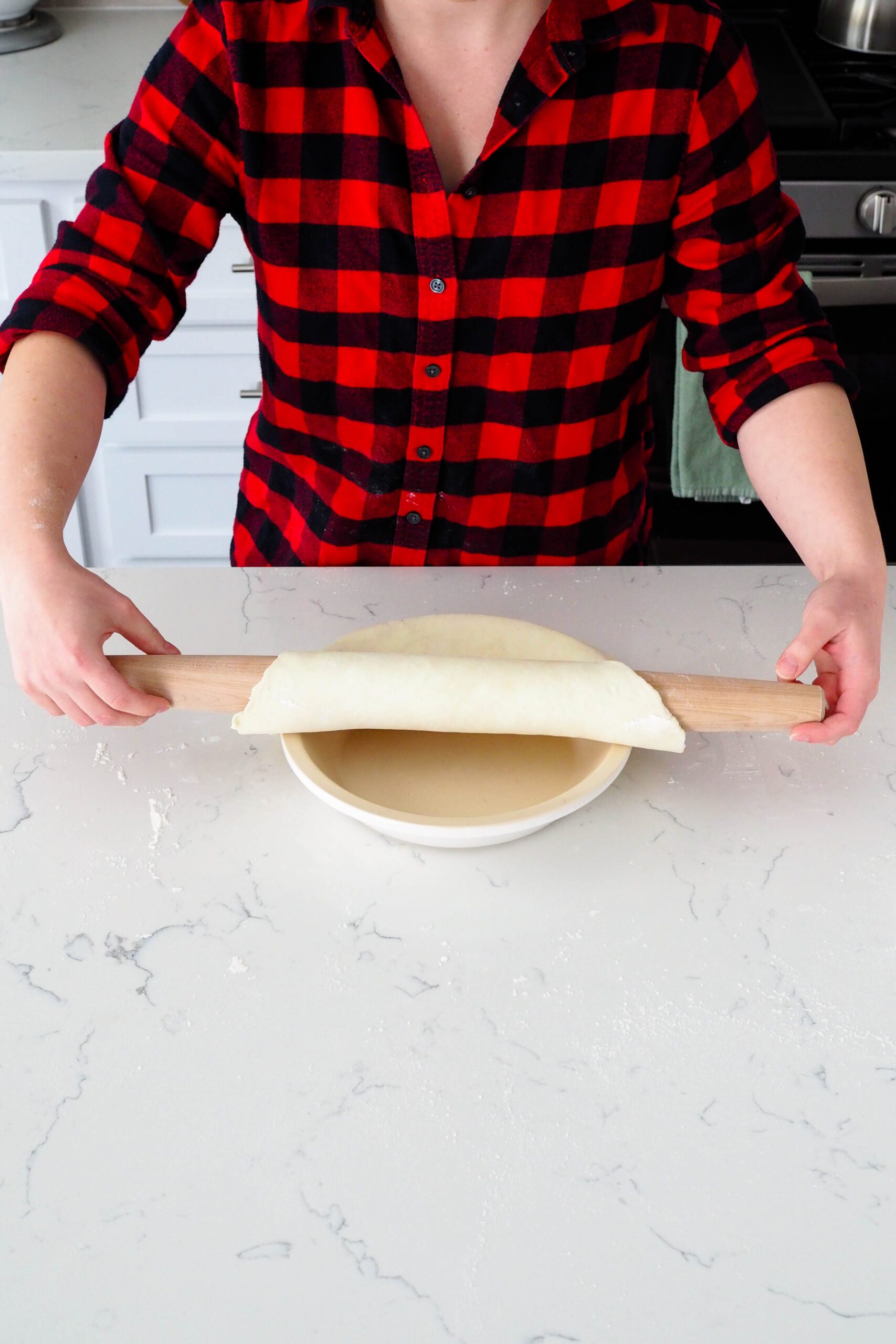 A woman unrolls pie dough into a pie pan.