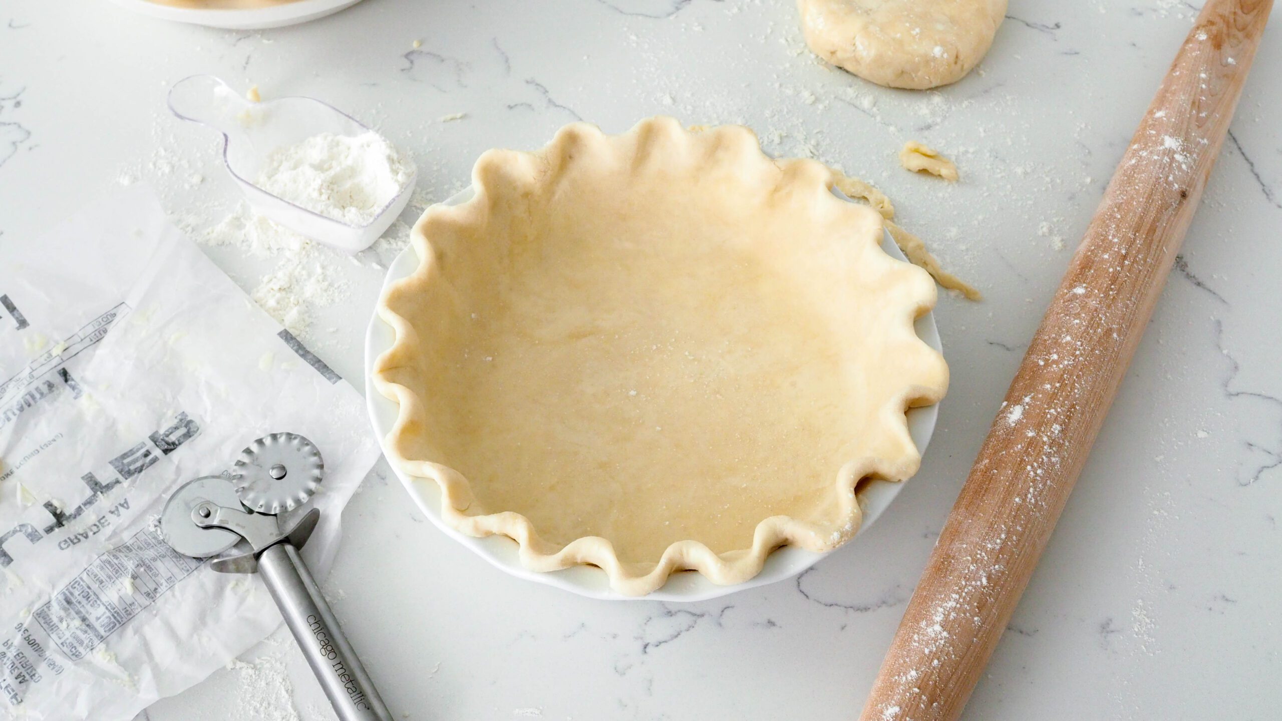 A fluted, unbaked pie crust next to a rolling pin and pastry wheel.