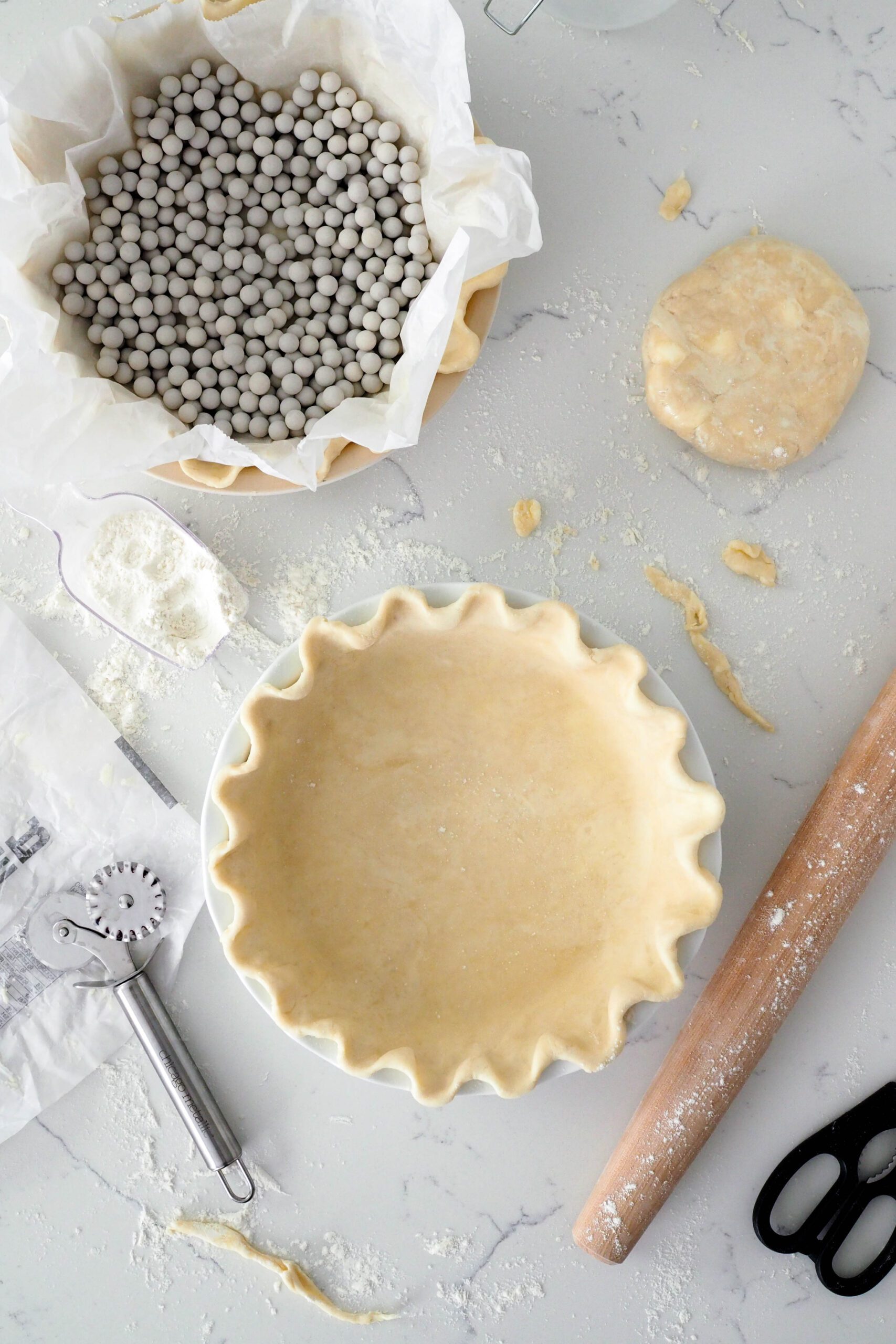 A fluted, unbaked pie crust next to another pie crust filled with ceramic pie weights.
