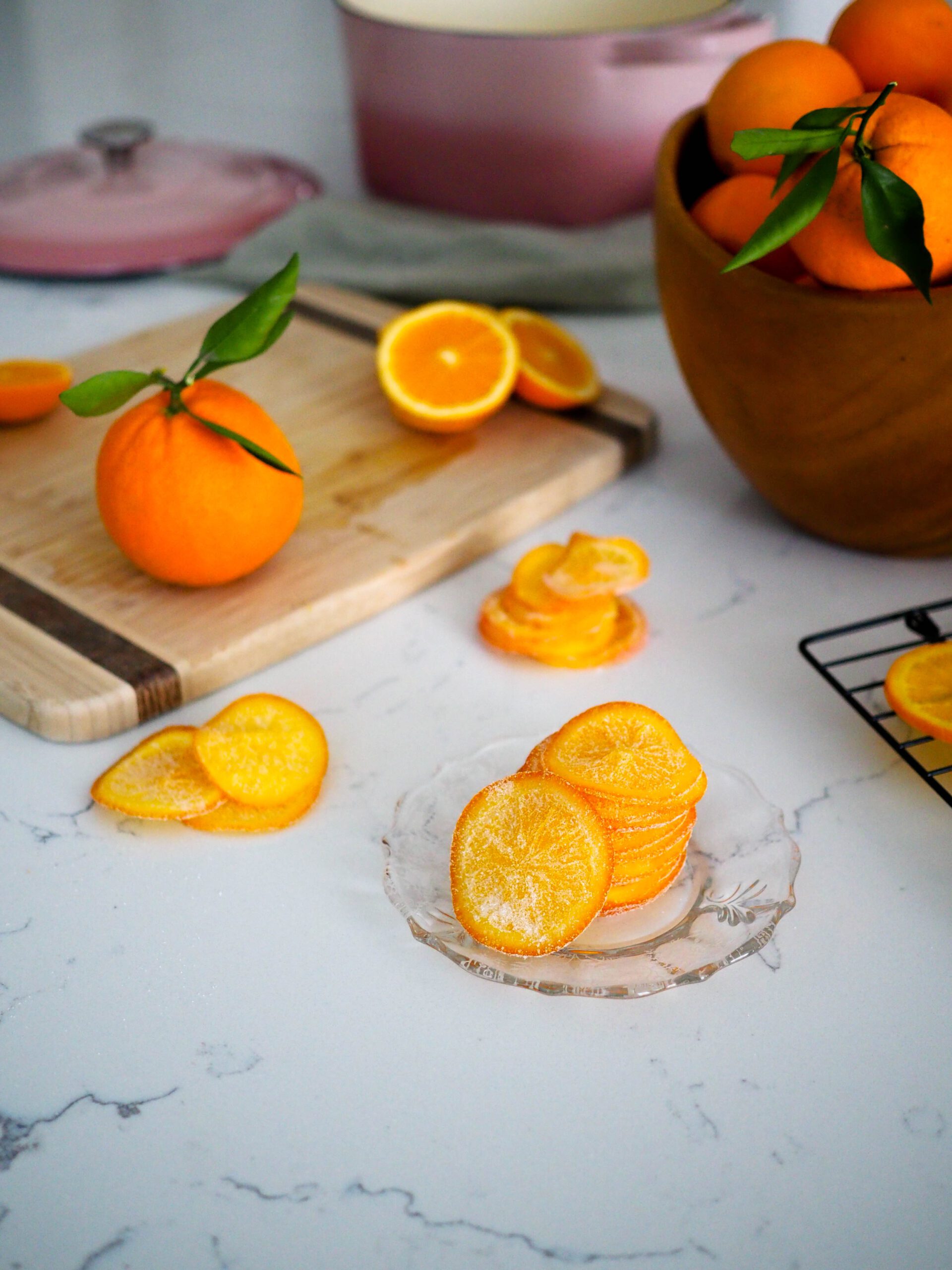 A stack of candied orange slices on a glass plate with styled oranges around it.