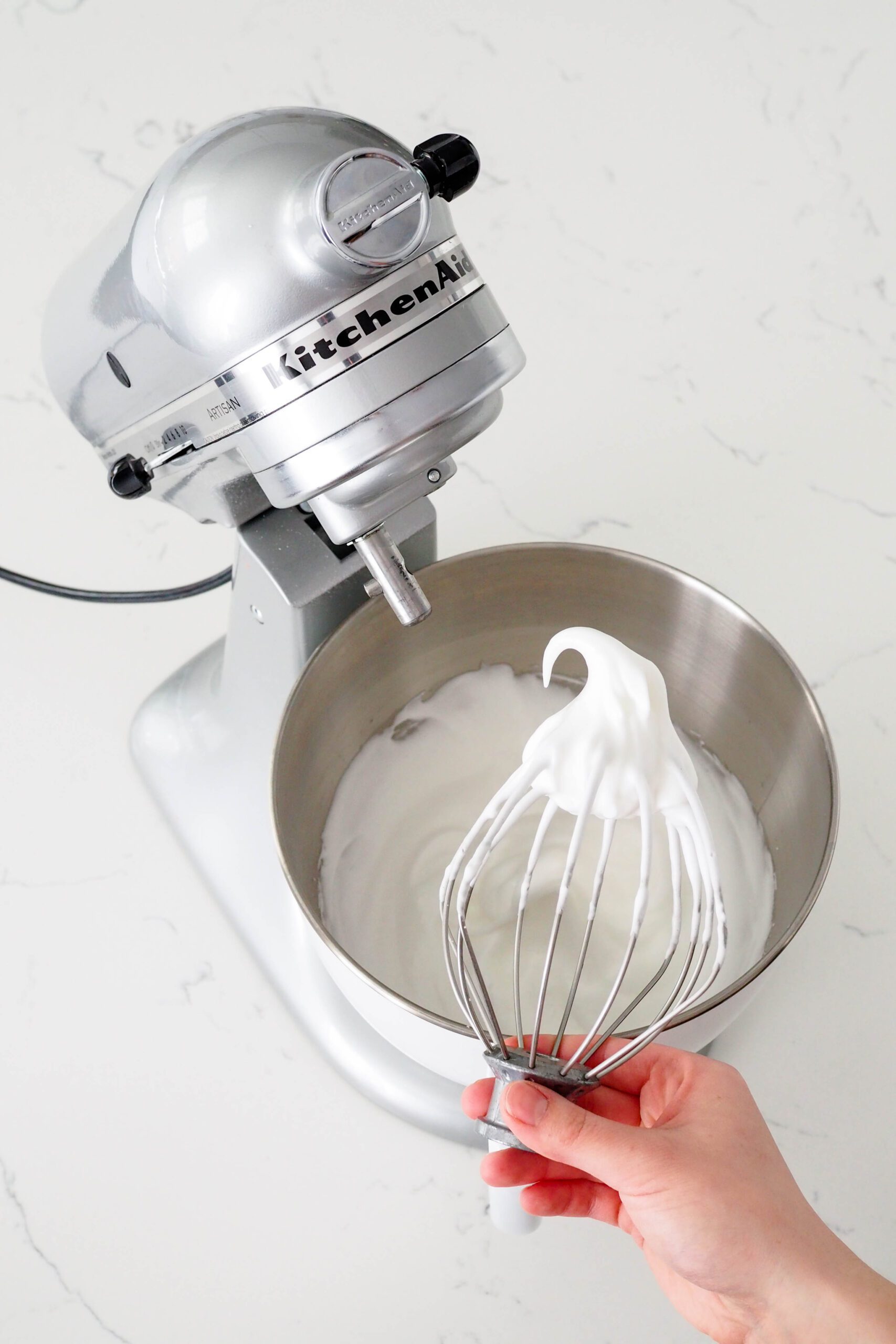 A whisk attachment is upended, showing a clump of meringue with soft peaks.