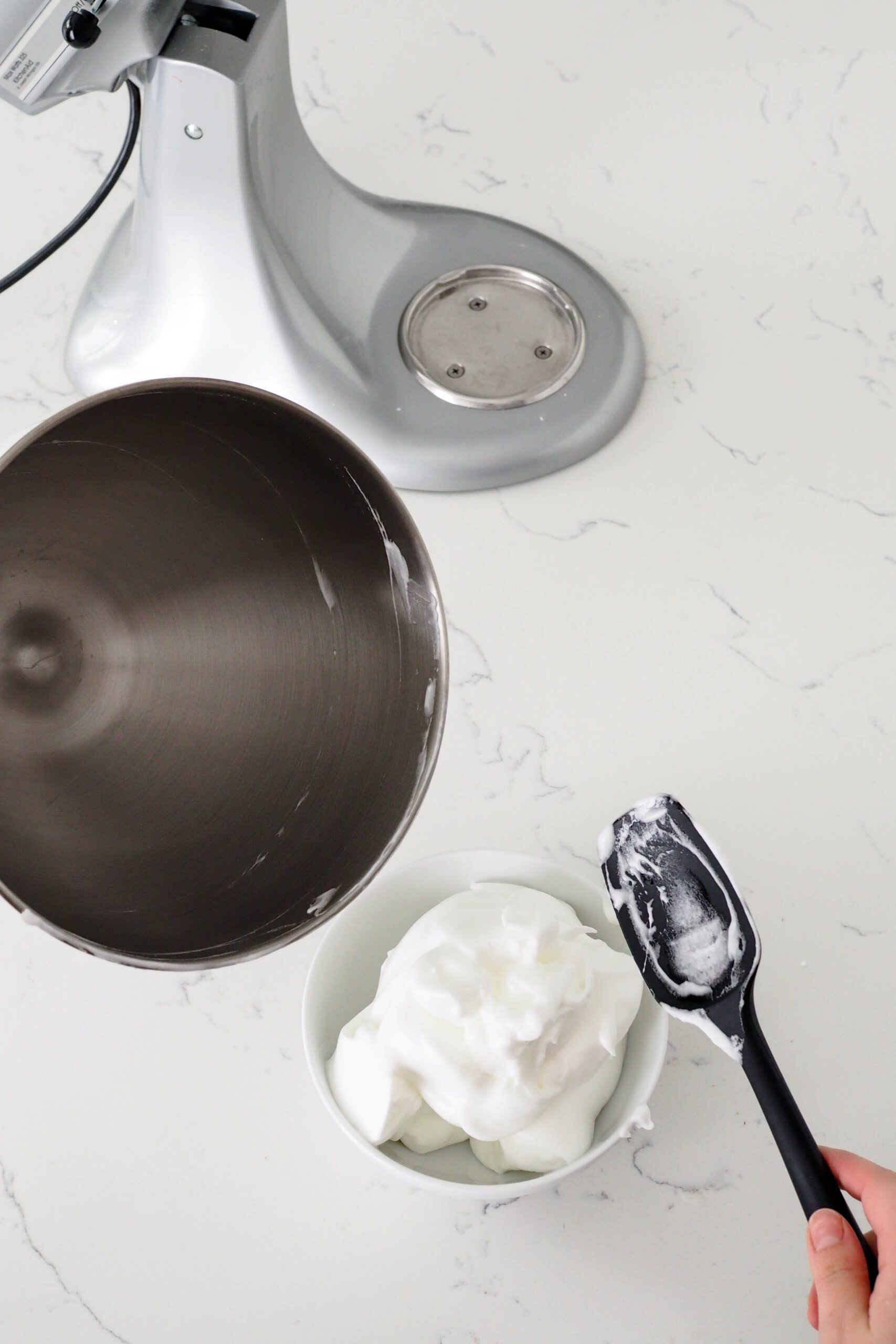 Meringue is scraped out of a mixer bowl into another medium bowl, leaving a clean mixer bowl.