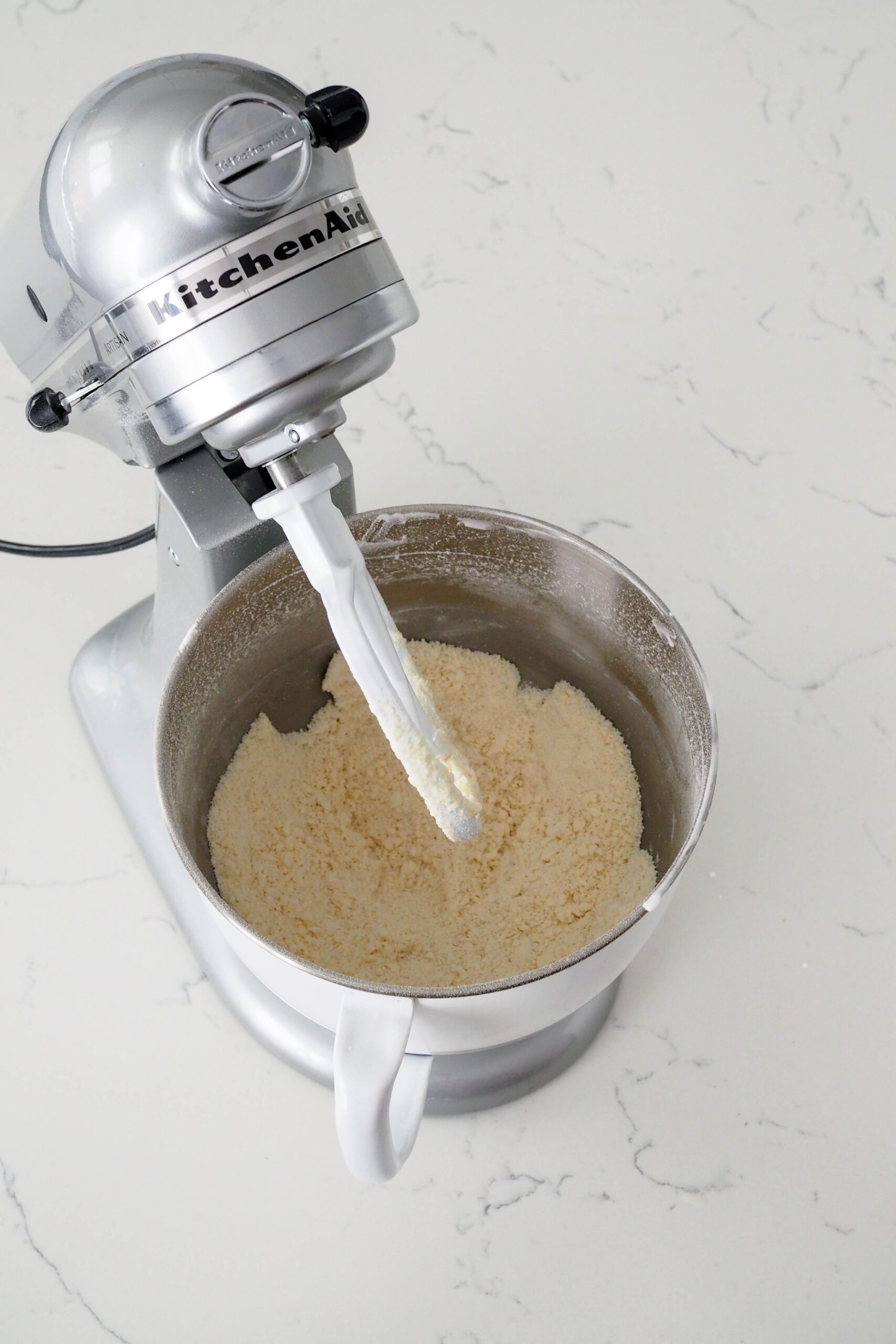 A mixer bowl has flour, sugar, butter, and leavening agents mixed together until they look like breadcrumbs.