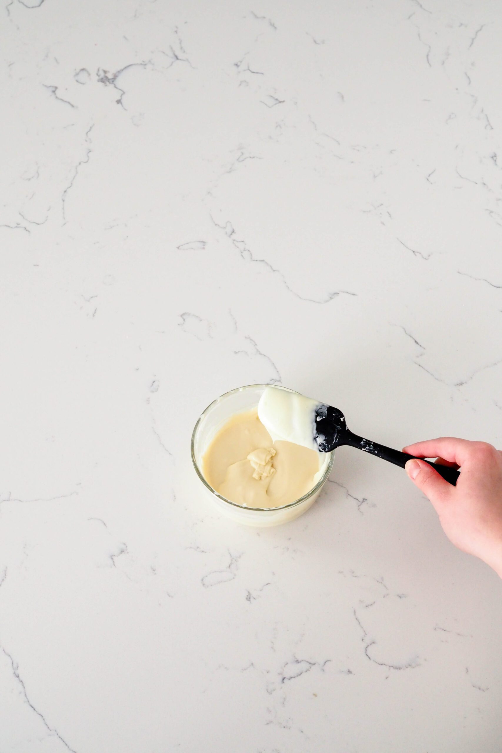 A spatula drizzles melted white chocolate into a bowl.