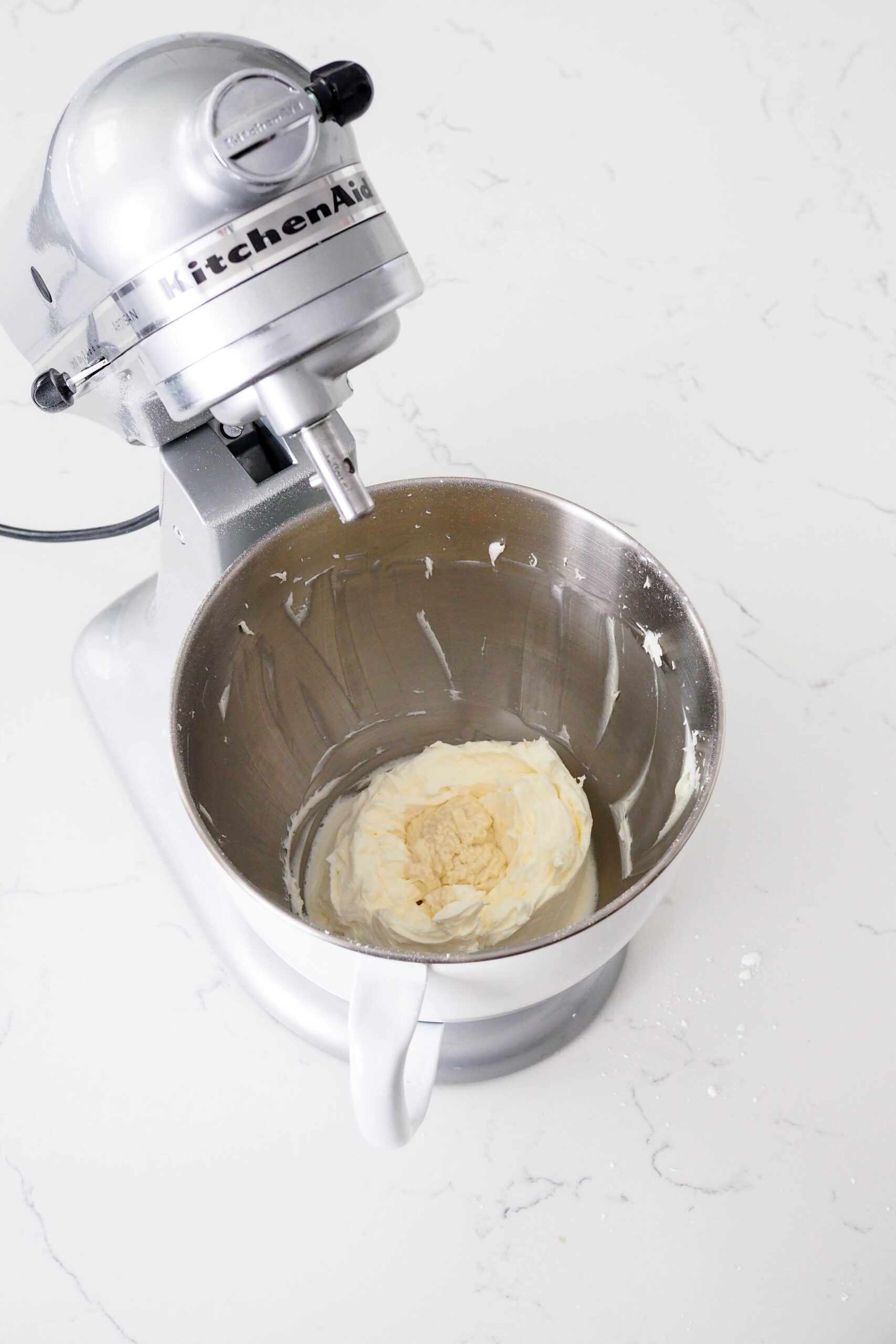 White chocolate is in a well inside of buttercream in a mixer bowl.