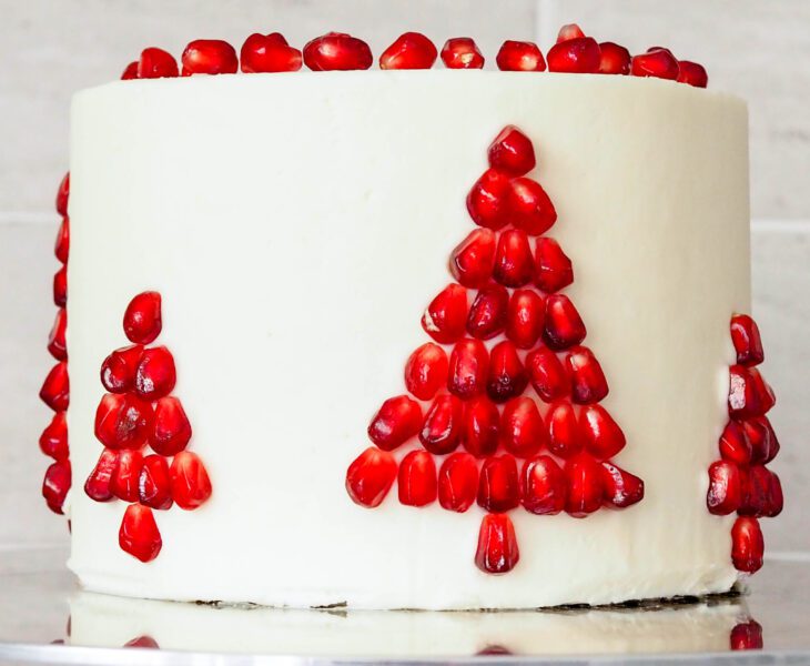 White chocolate pomegranate layer cake has a Christmas tree made out of pomegranate arils on the side.
