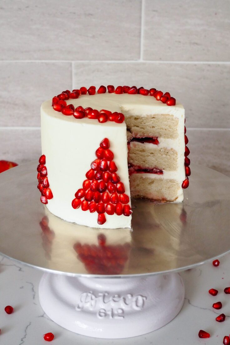 A Christmas tree made of pomegranate arils is on the side of a white chocolate pomegranate layer cake.