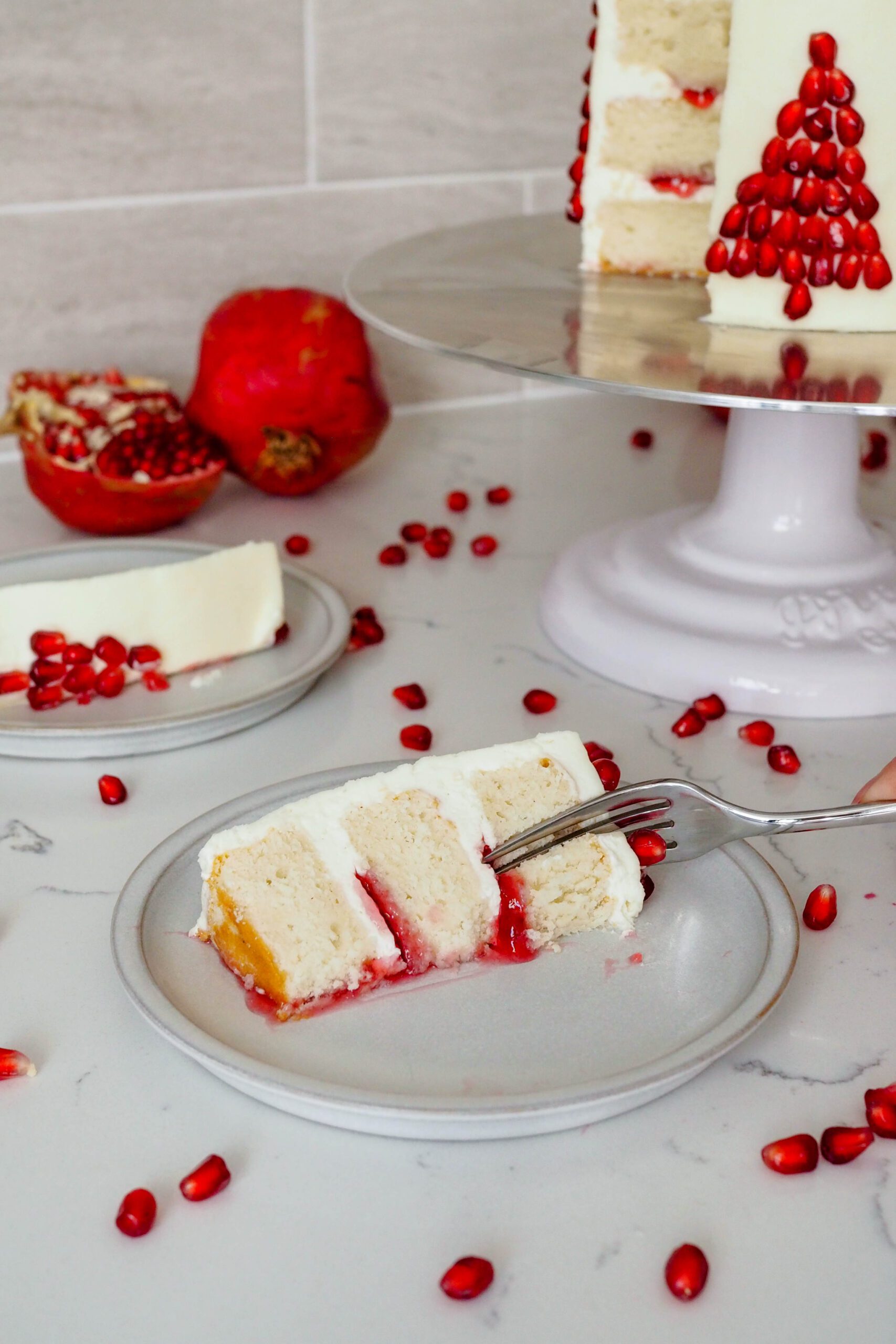 A fork cuts into a slice of white cake with white chocolate buttercream and pomegranate filling.
