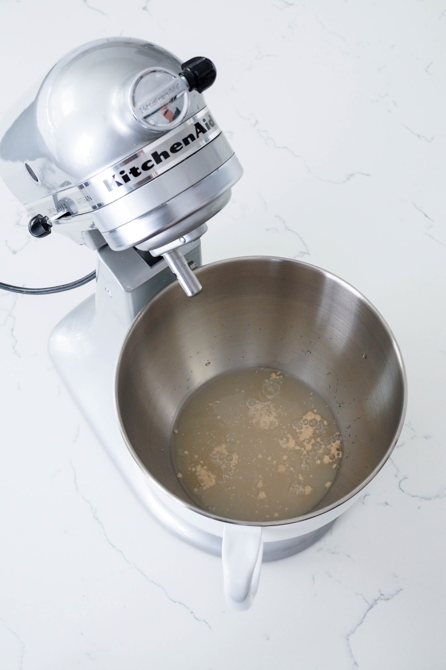 Yeast dissolves in water in a stand mixer bowl.