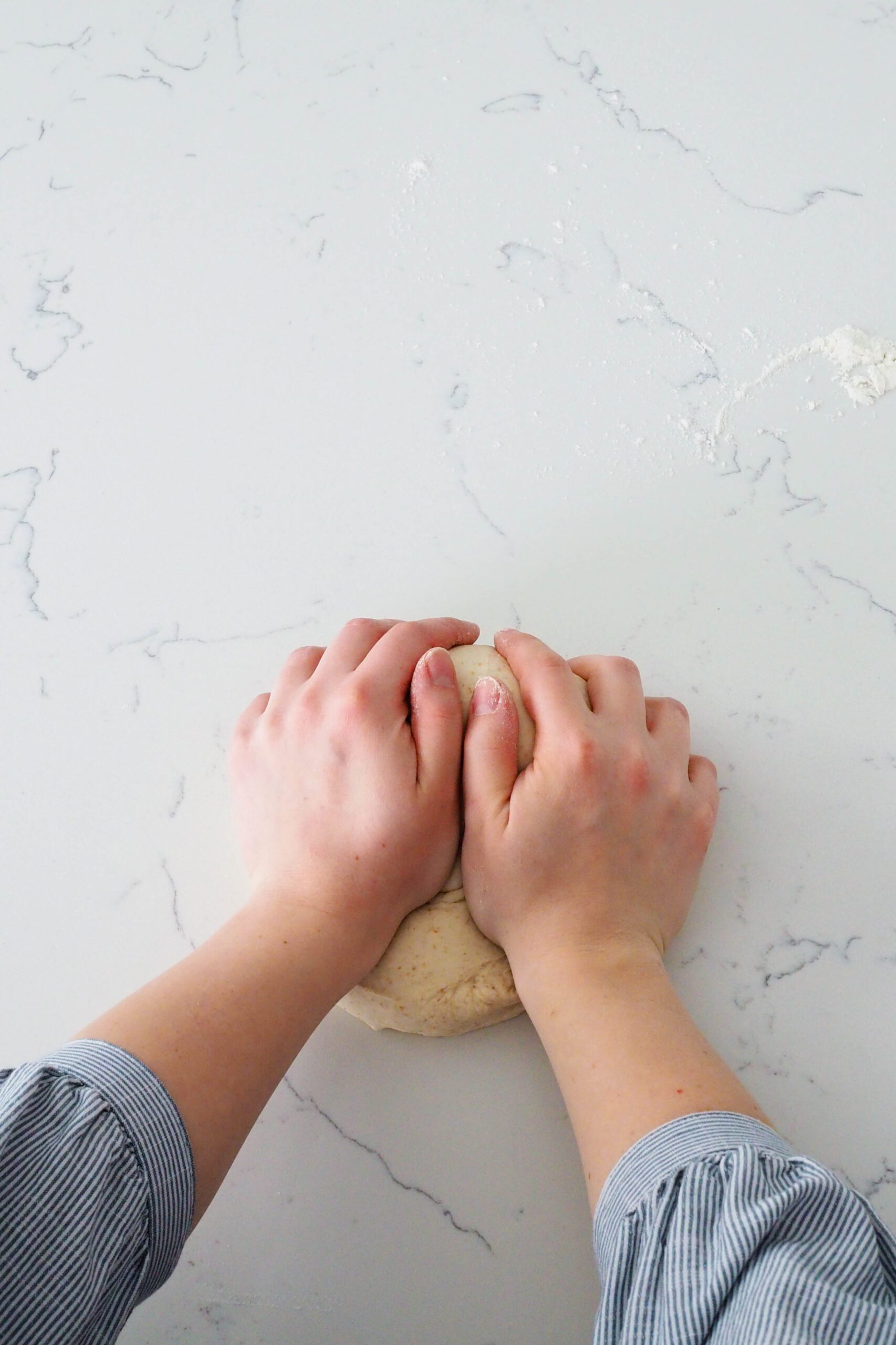 Two hands knead a ball of thin crust pizza dough.