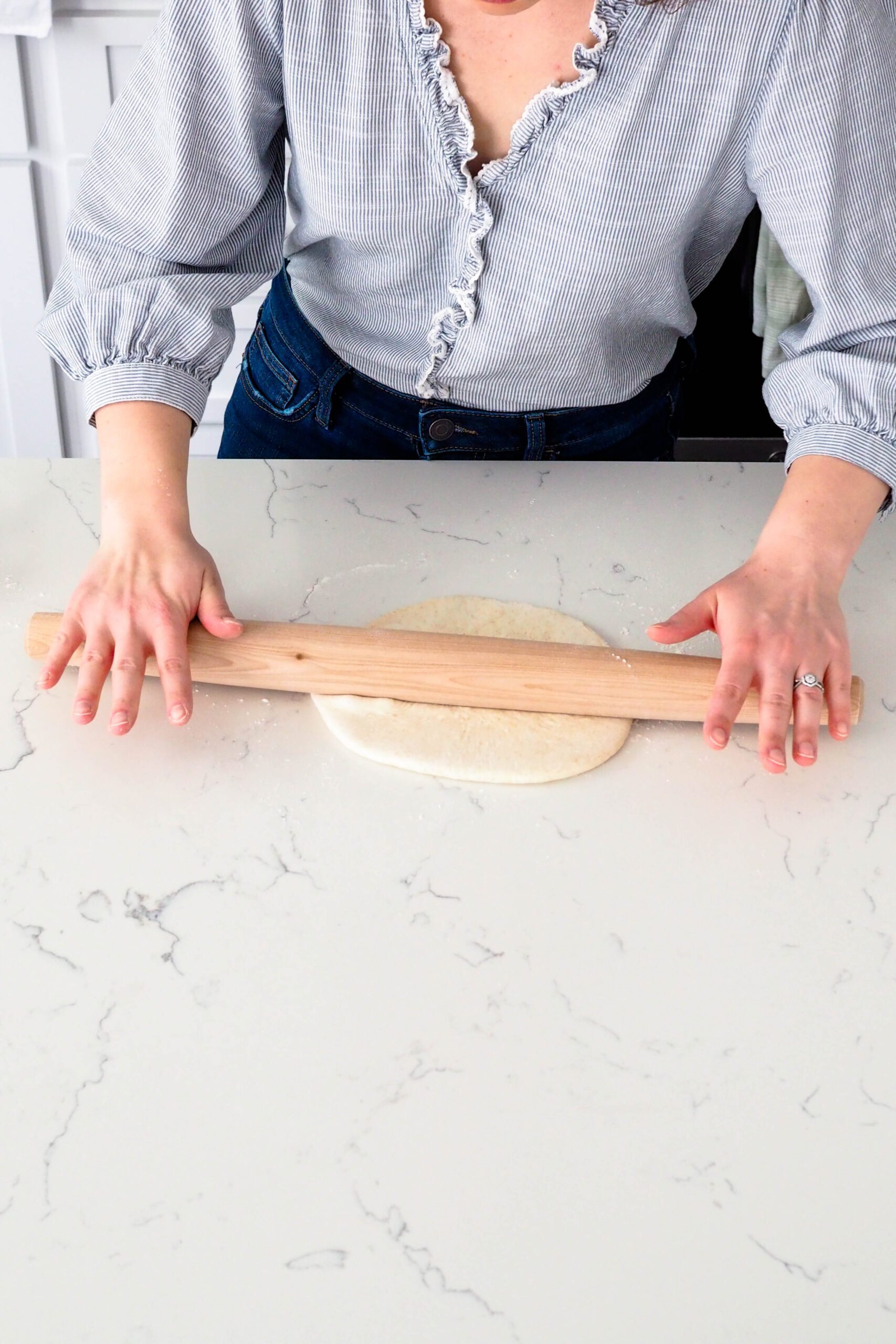Two hands roll out a round of thin crust pizza dough.