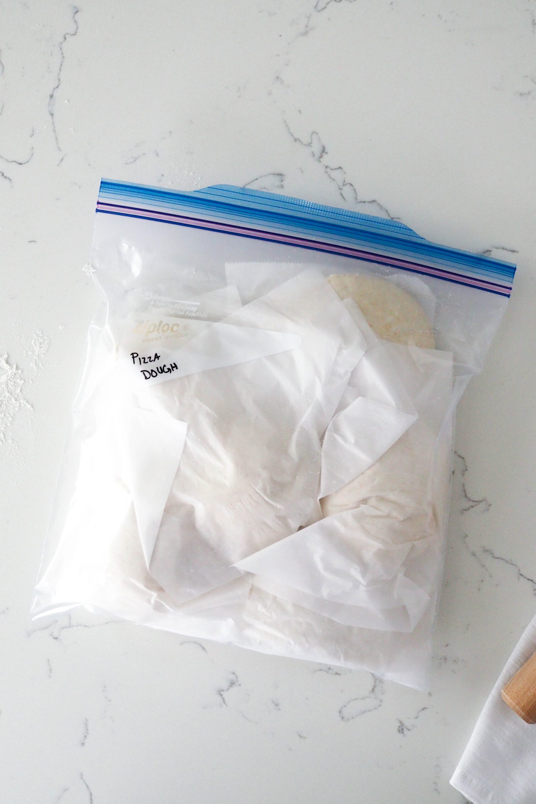 A gallon-sized freezer Ziploc bag has balls of dough wrapped in parchment inside it.