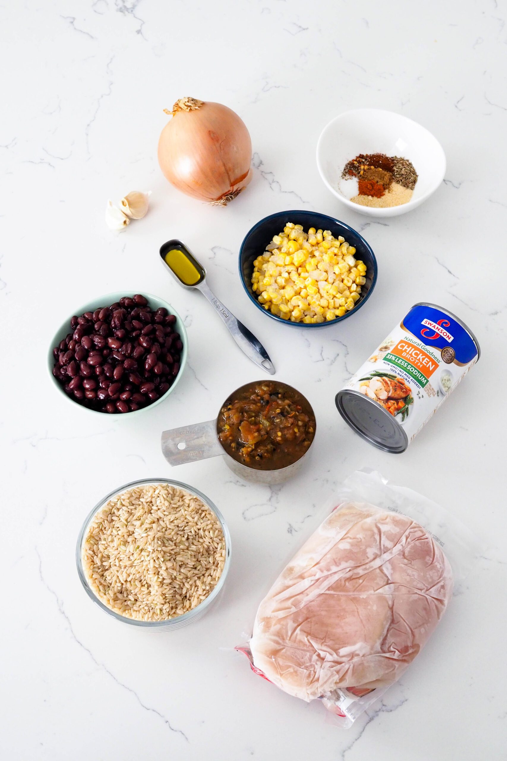The ingredients for one-pot chicken and brown rice on a quartz countertop.