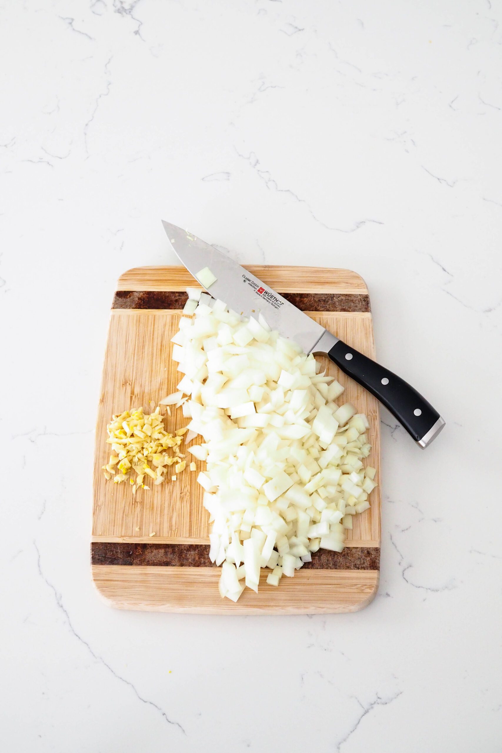 Diced onion and minced garlic on a cutting board with a knife.