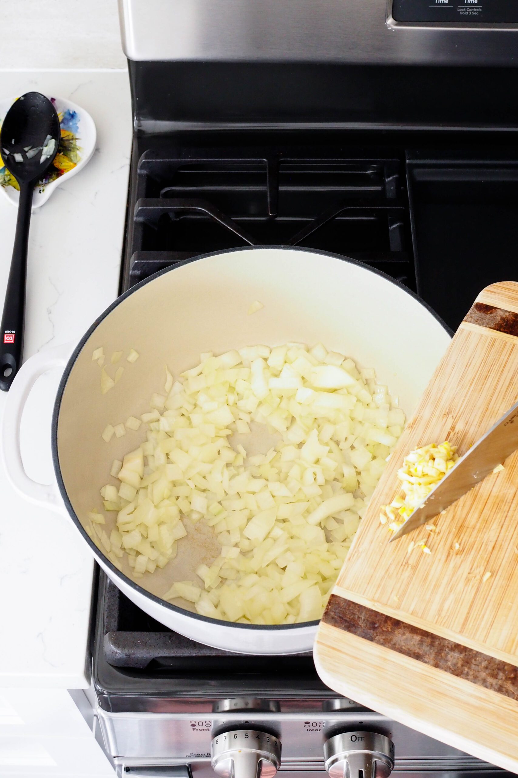 A knife slides minced garlic into the Dutch oven once the onions have softened.
