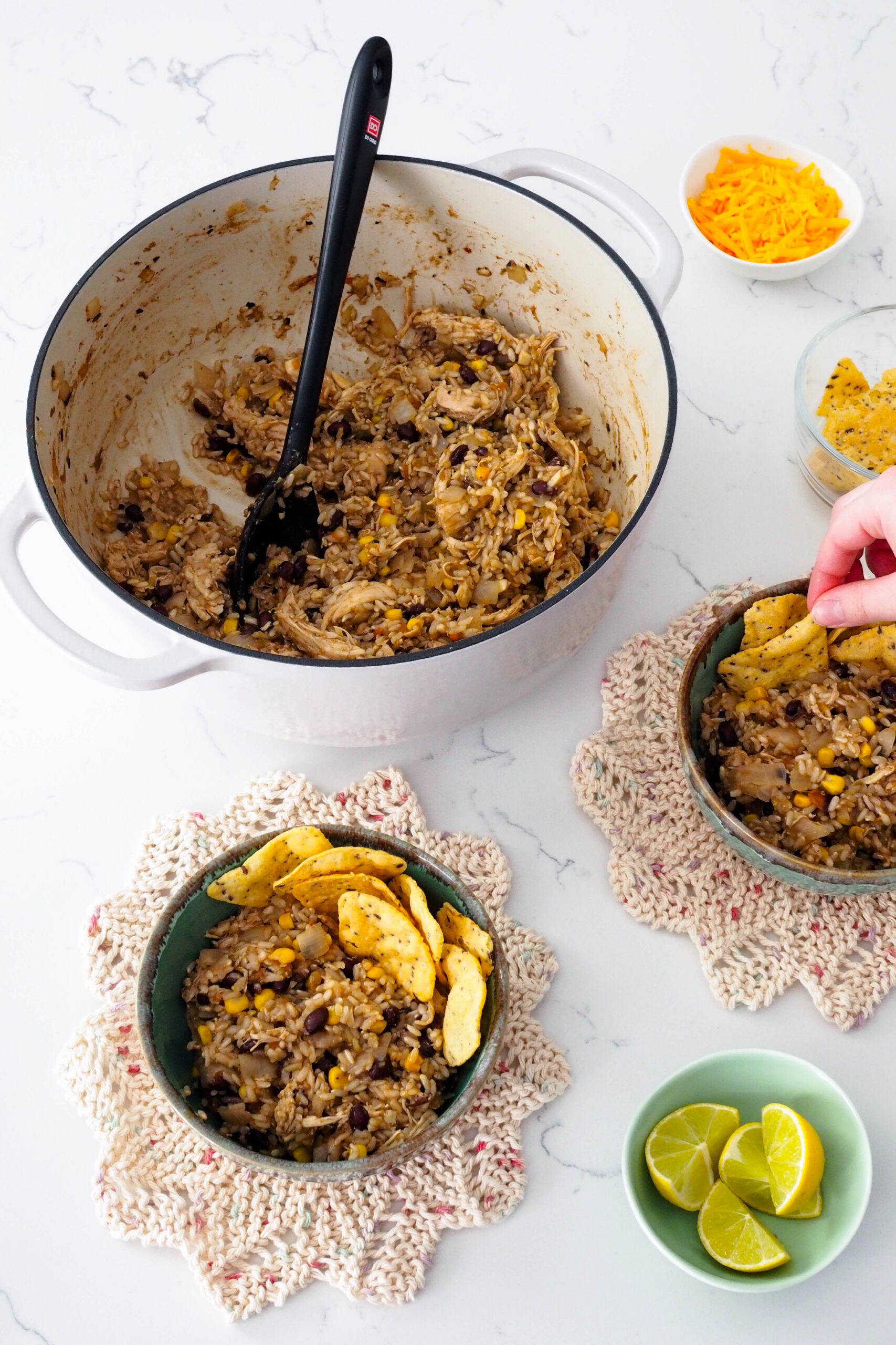 A hand adds tortilla chips to a bowl of one-pot chicken and brown rice.