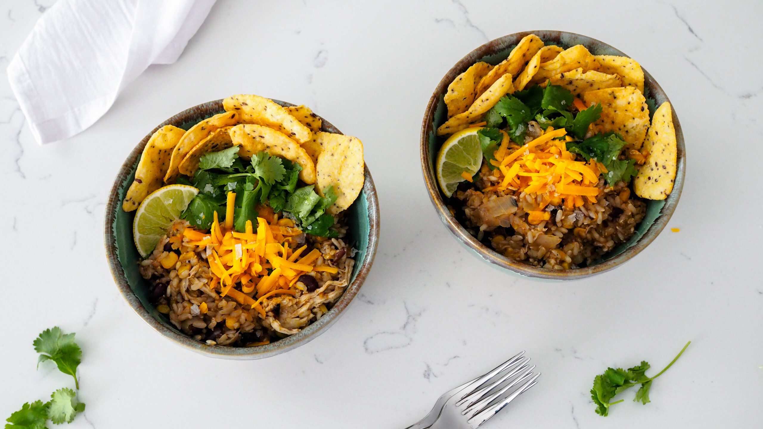 Two bowls of one-pot chicken and brown rice with toppings.