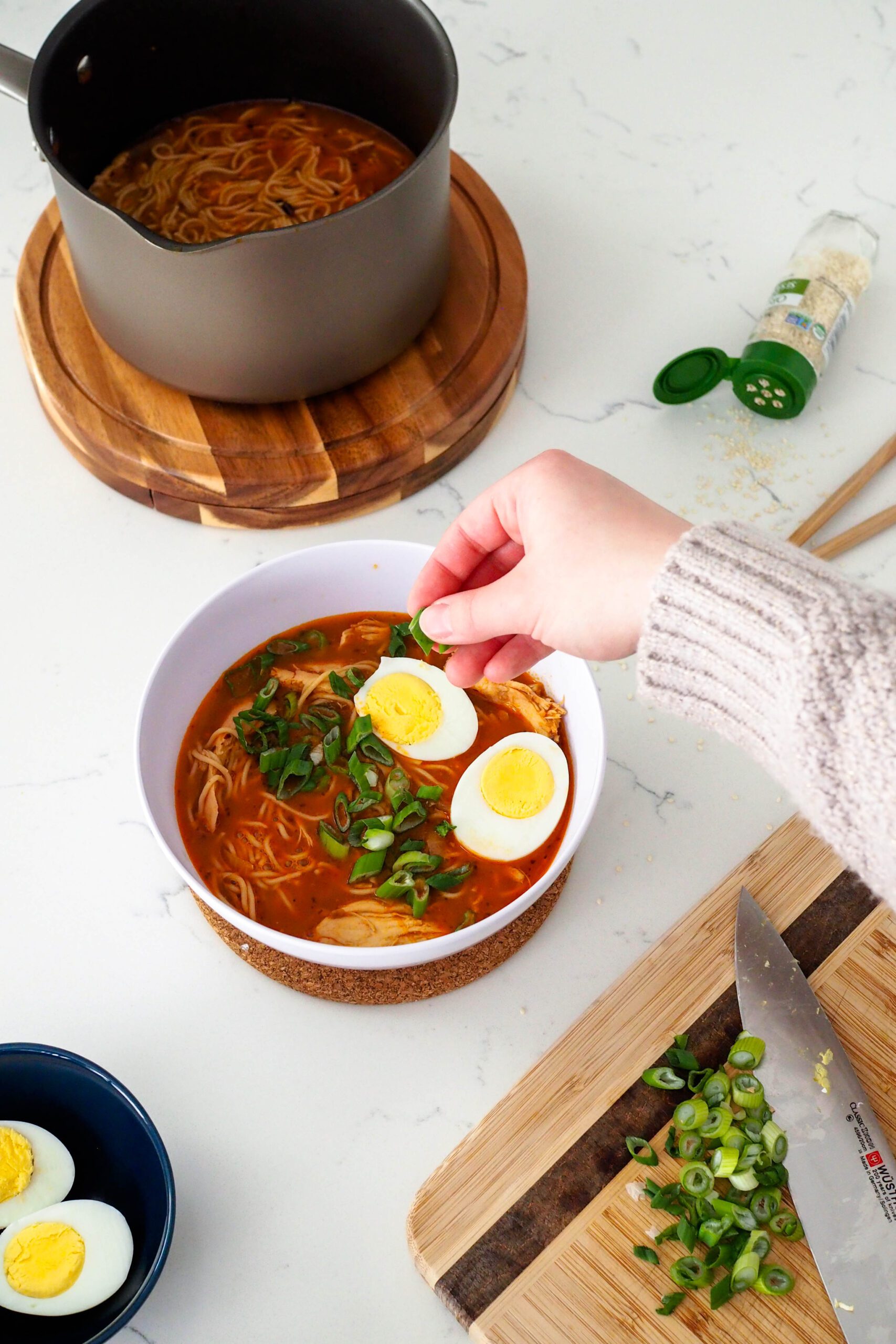 A hand adds sliced green onions on top of gochujang ramen.