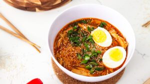 A bowl of gochujang chicken ramen with two halves of a boiled egg in it.
