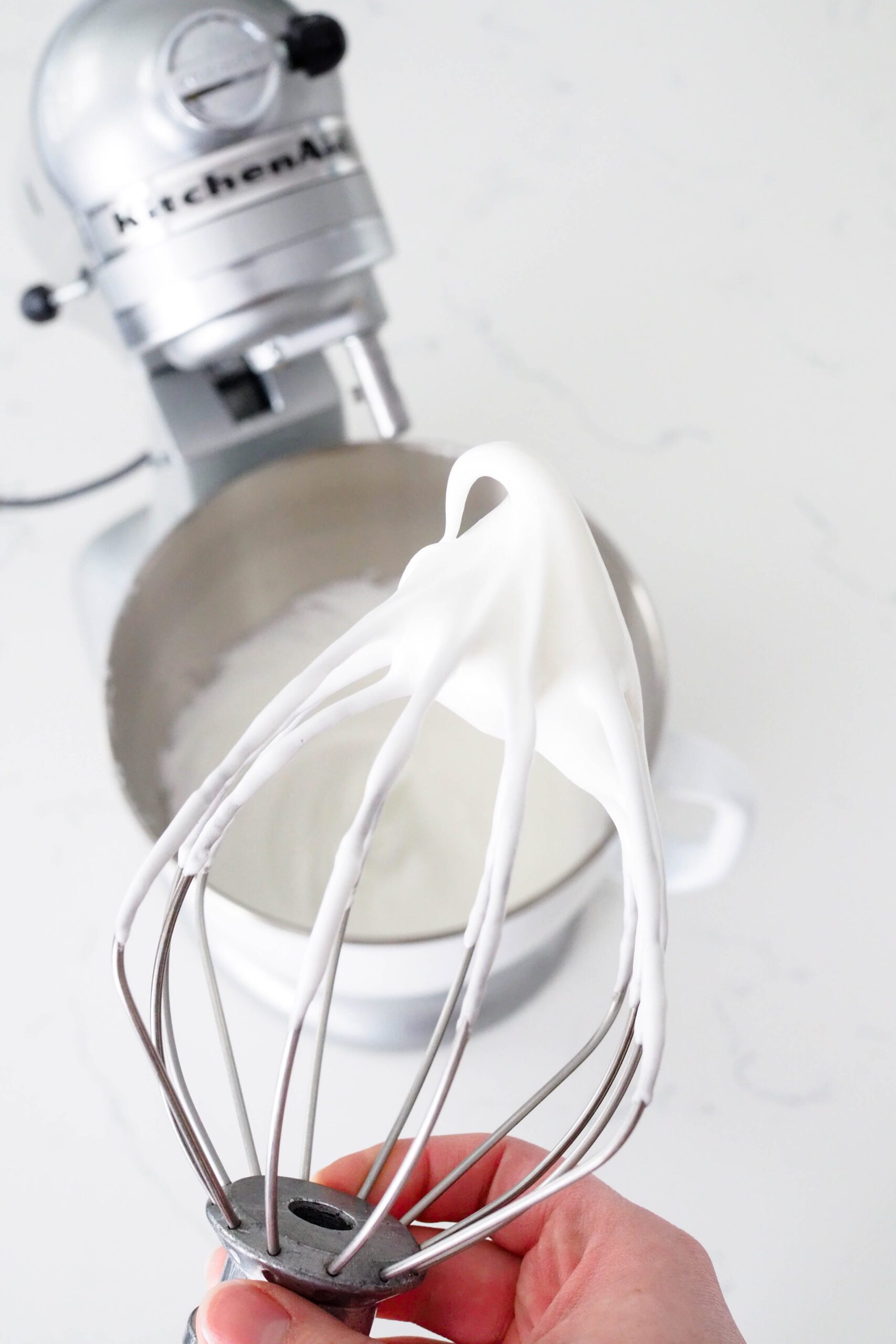 A whisk attachment is held up with a clump of soft-peaked meringue to add to the batter for mini confetti layer cakes.