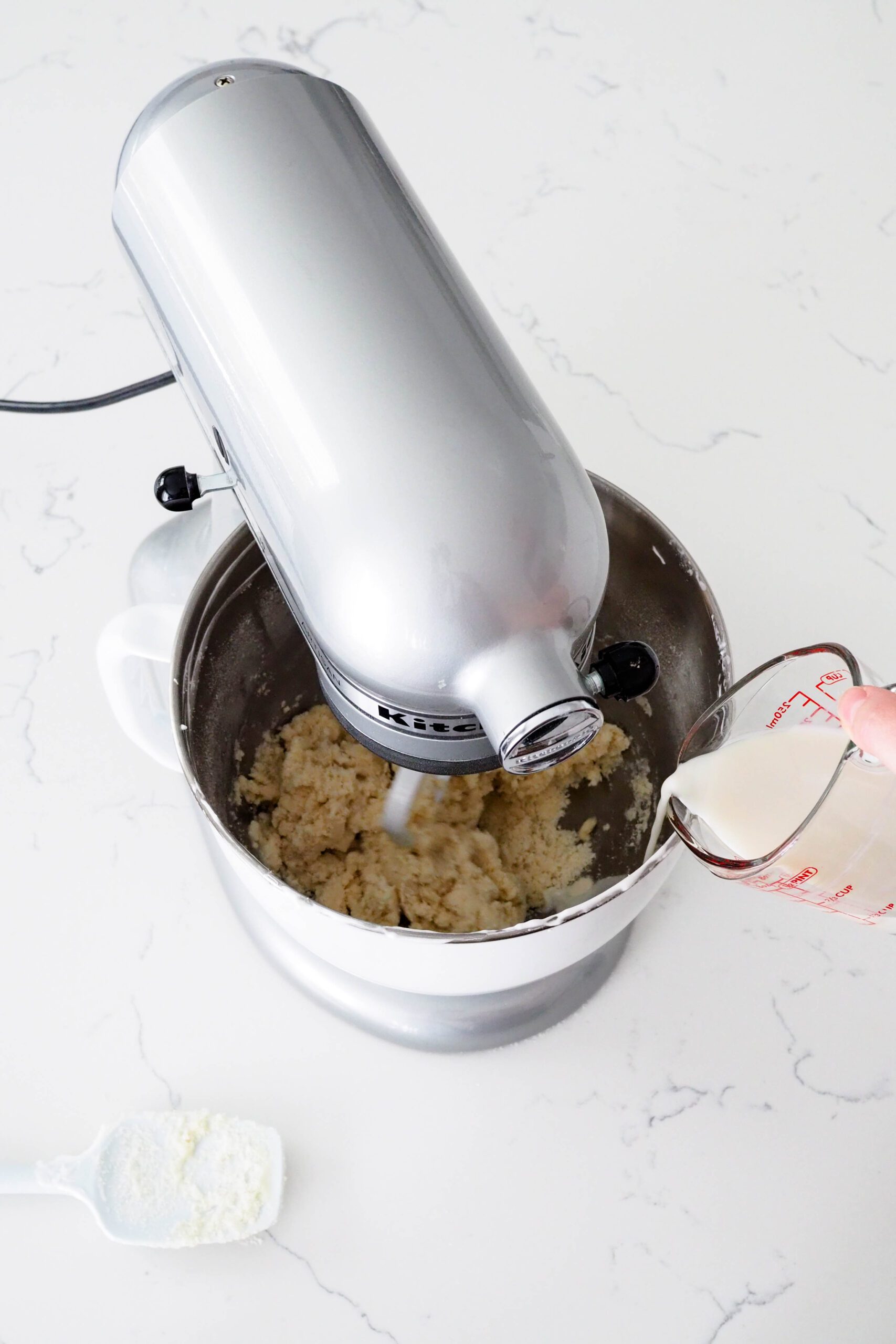 Milk is streamed into a mixing bowl with what appears to be breadcrumbs inside.