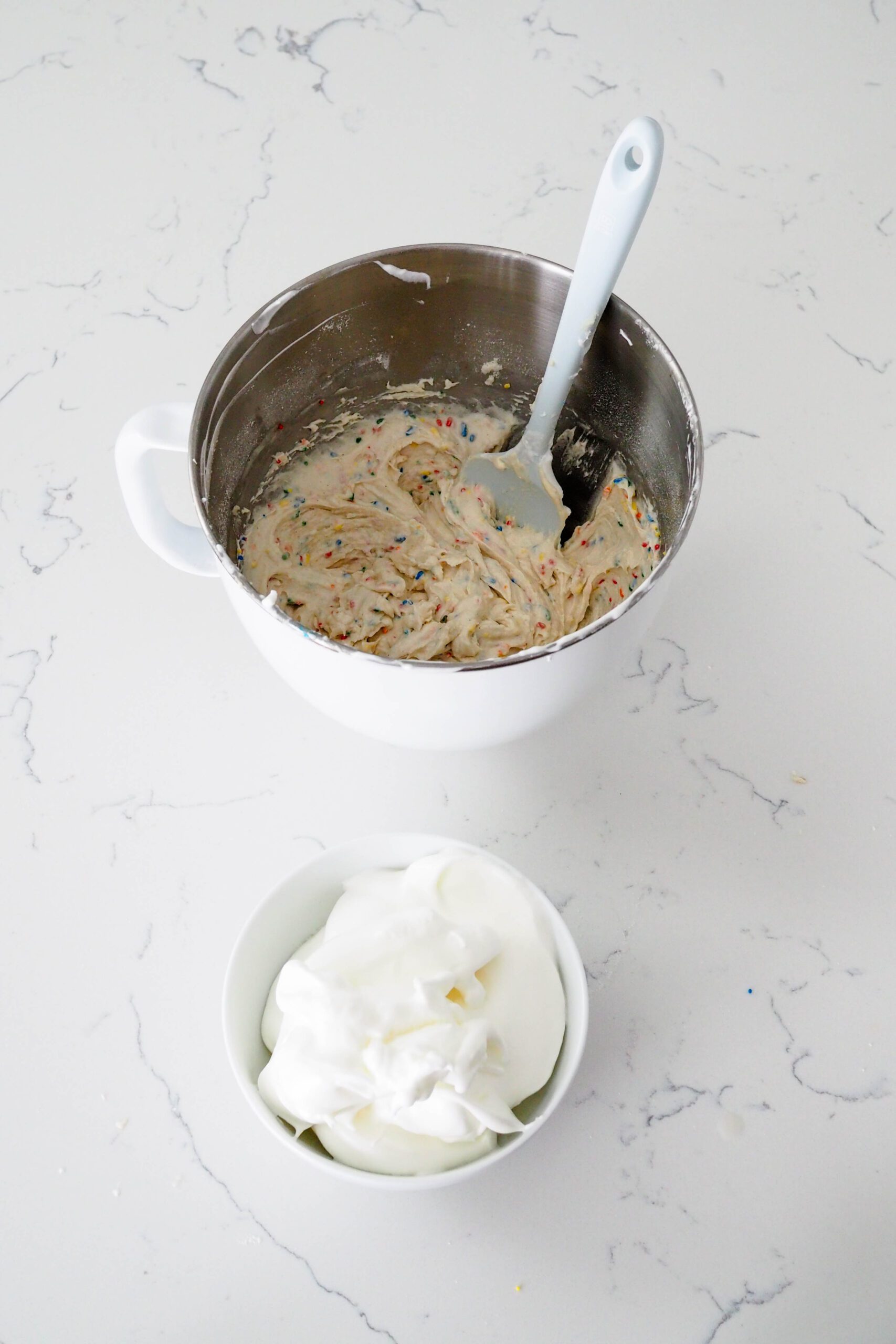 A mixing bowl with mini confetti layer cake batter above a bowl full of meringue.