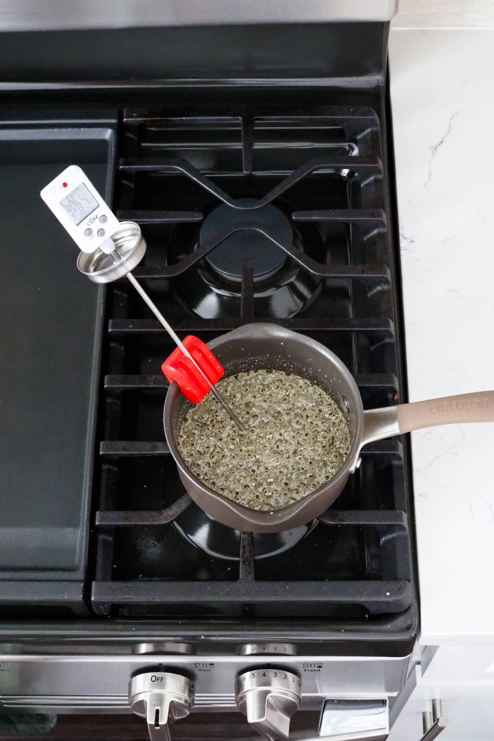 A candy thermometer rests on the side of a small saucepan with bubbling syrup.