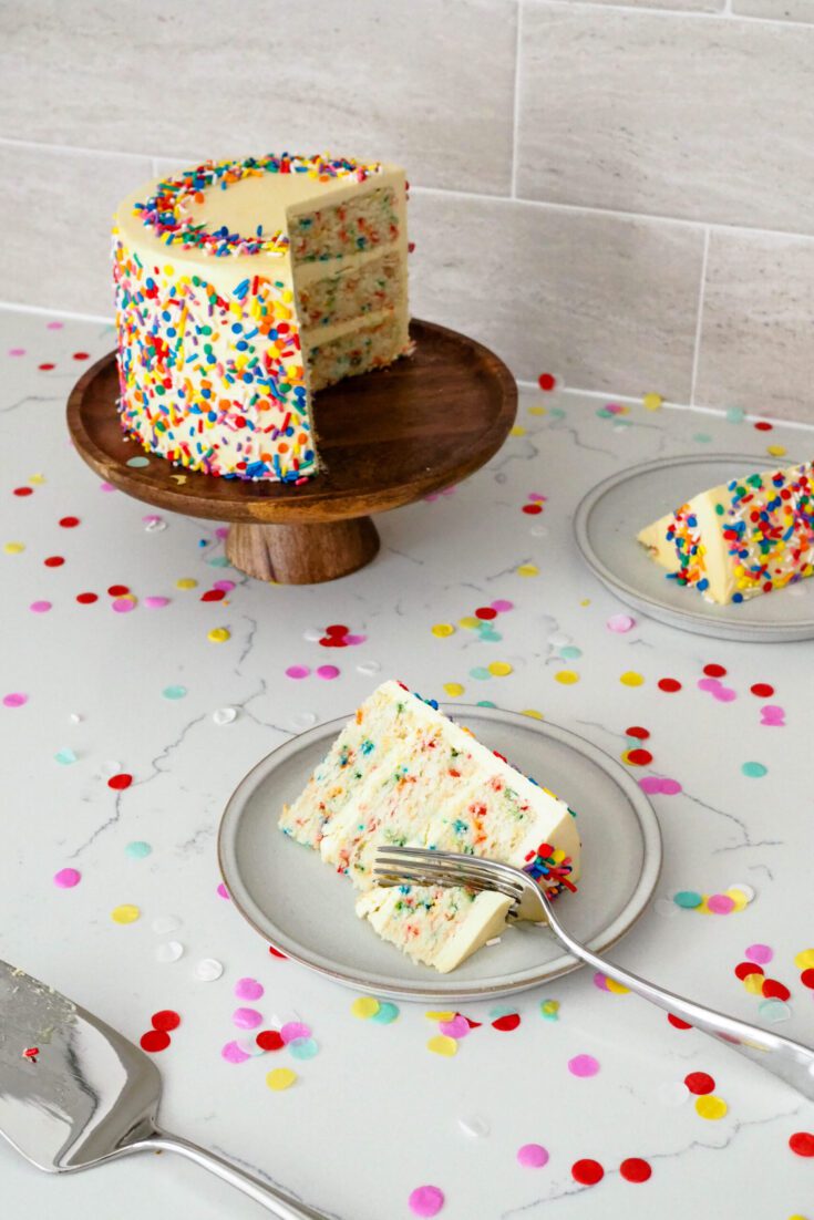 A slice of mini confetti layer cake has a fork taking a piece out of it.