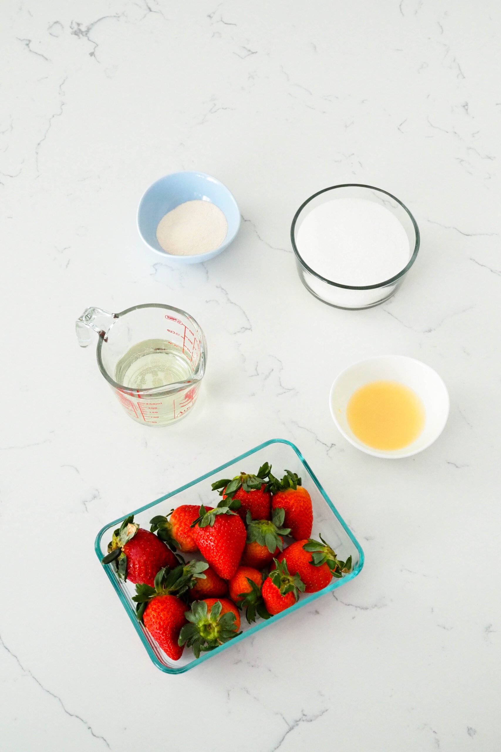 Pectin, sugar, lemon juice, strawberries, and champagne on a white quartz counter.
