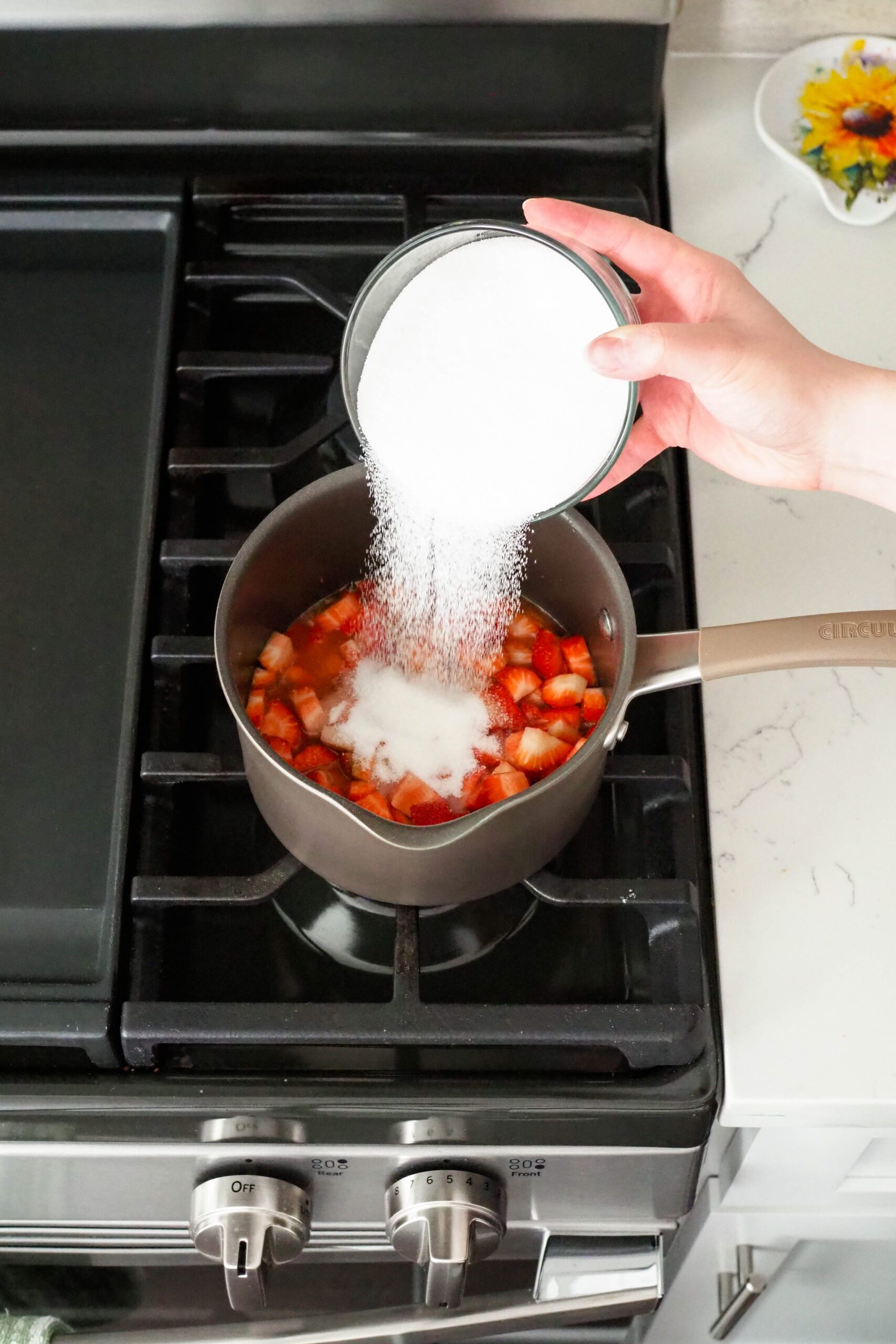 Sugar is poured into a saucepan with diced strawberries.