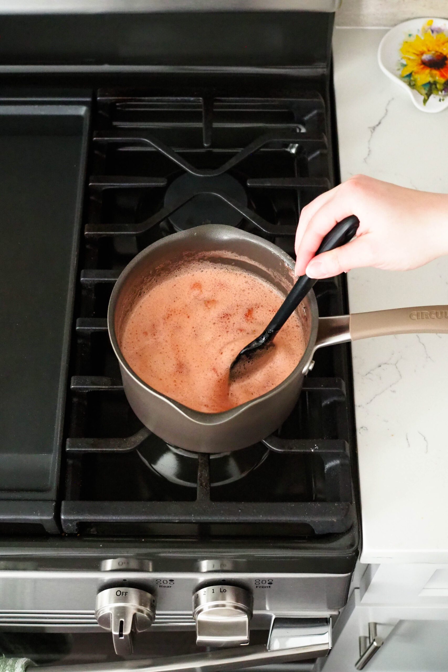 A black spatula stirs a pot of bubbling diced strawberries.