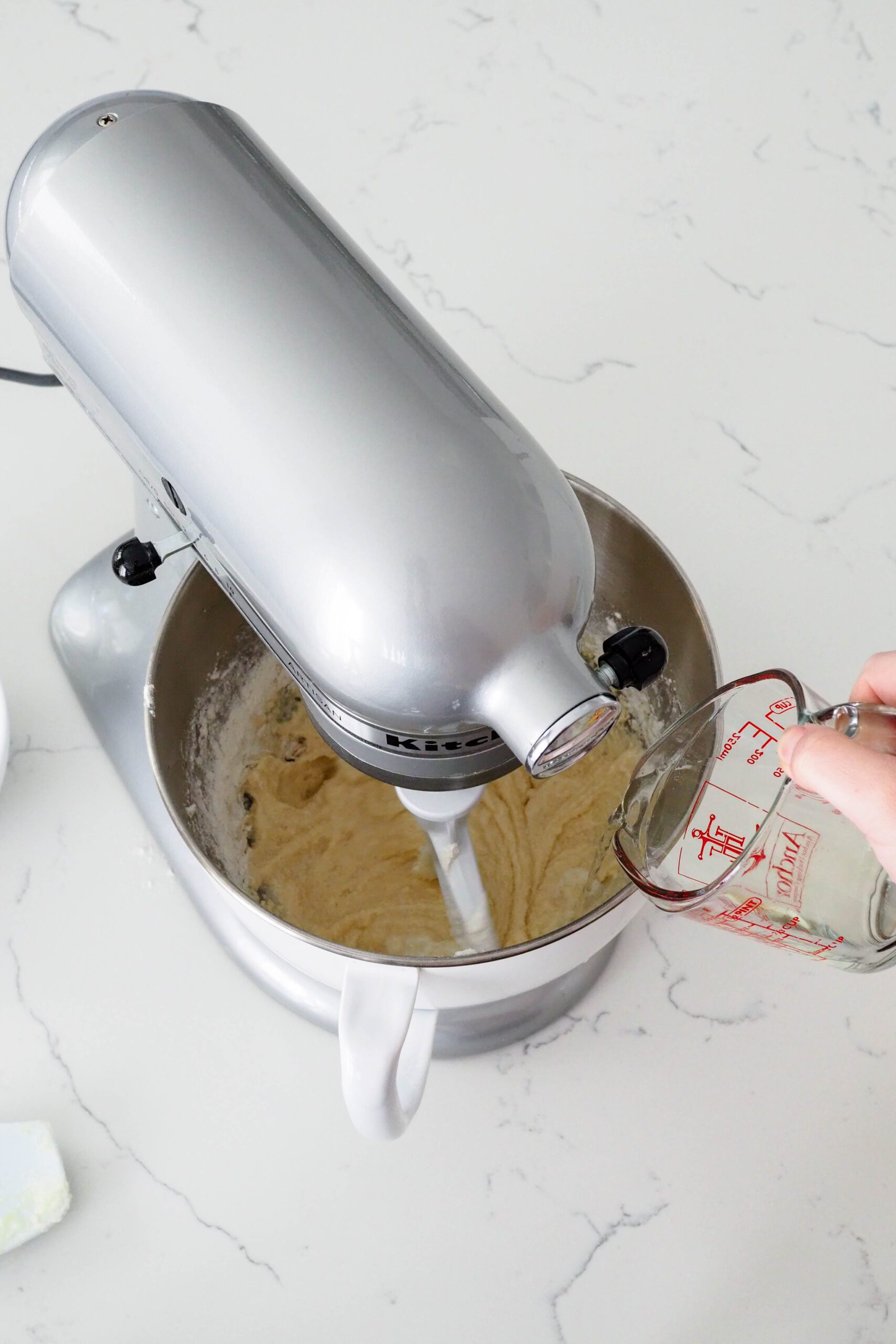 A measuring cup with champagne pours champagne into a stand mixer.