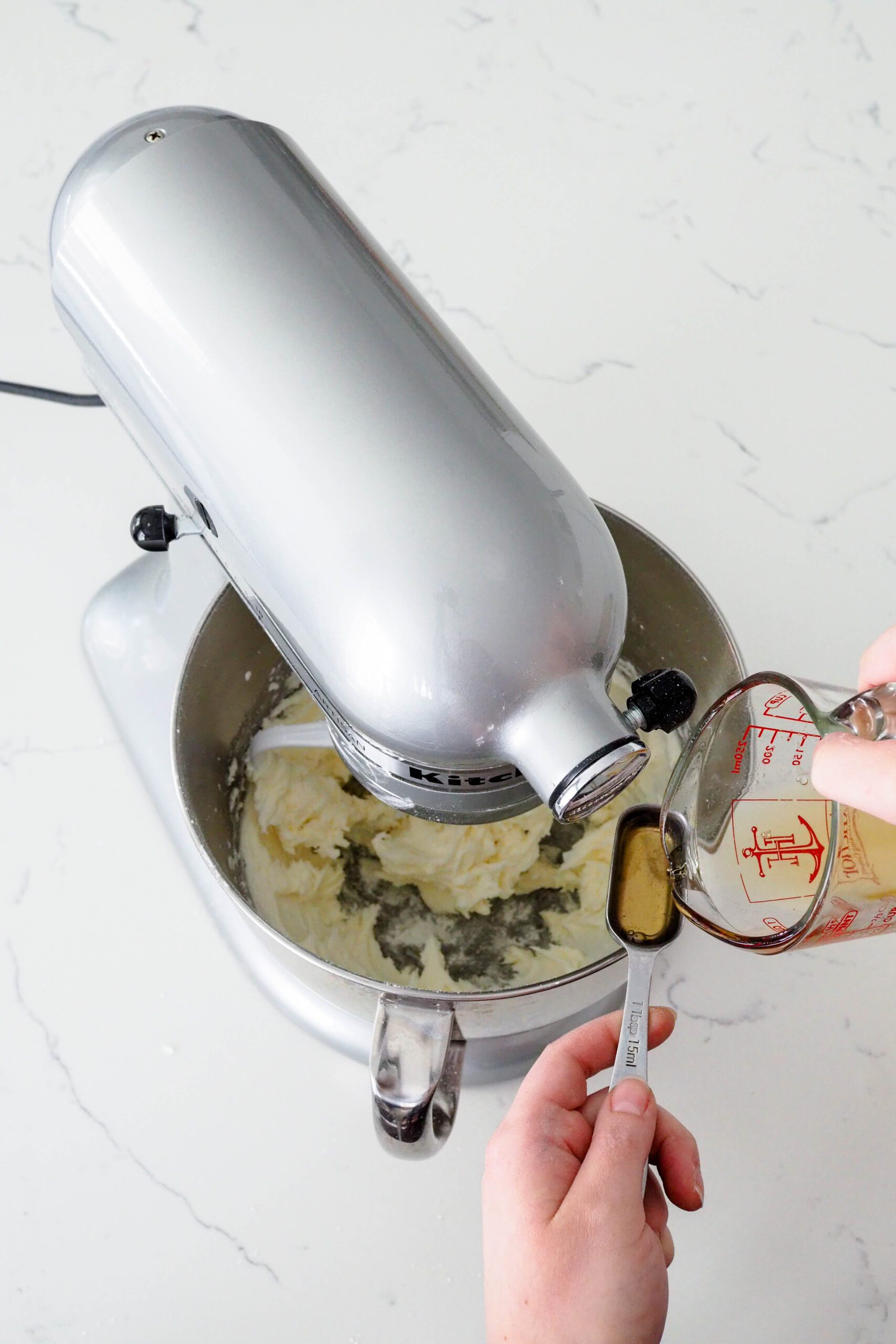 A measuring cup pours champagne reduction into a Tablespoon over a stand mixer bowl.