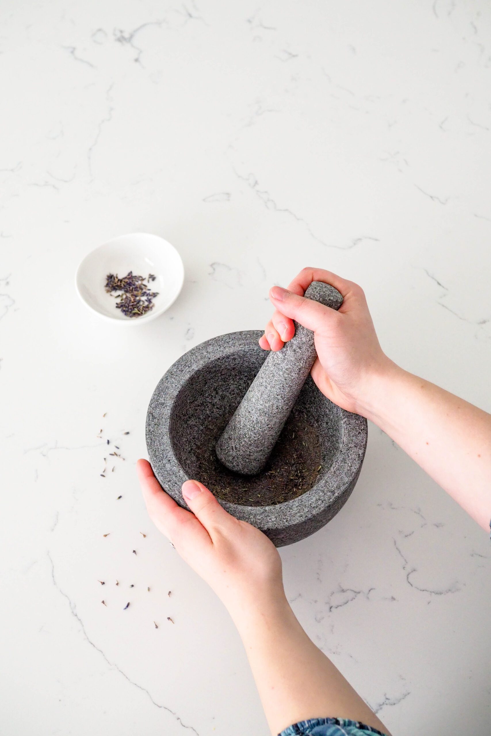 A hand grinds lavender buds in a mortar and pestle.