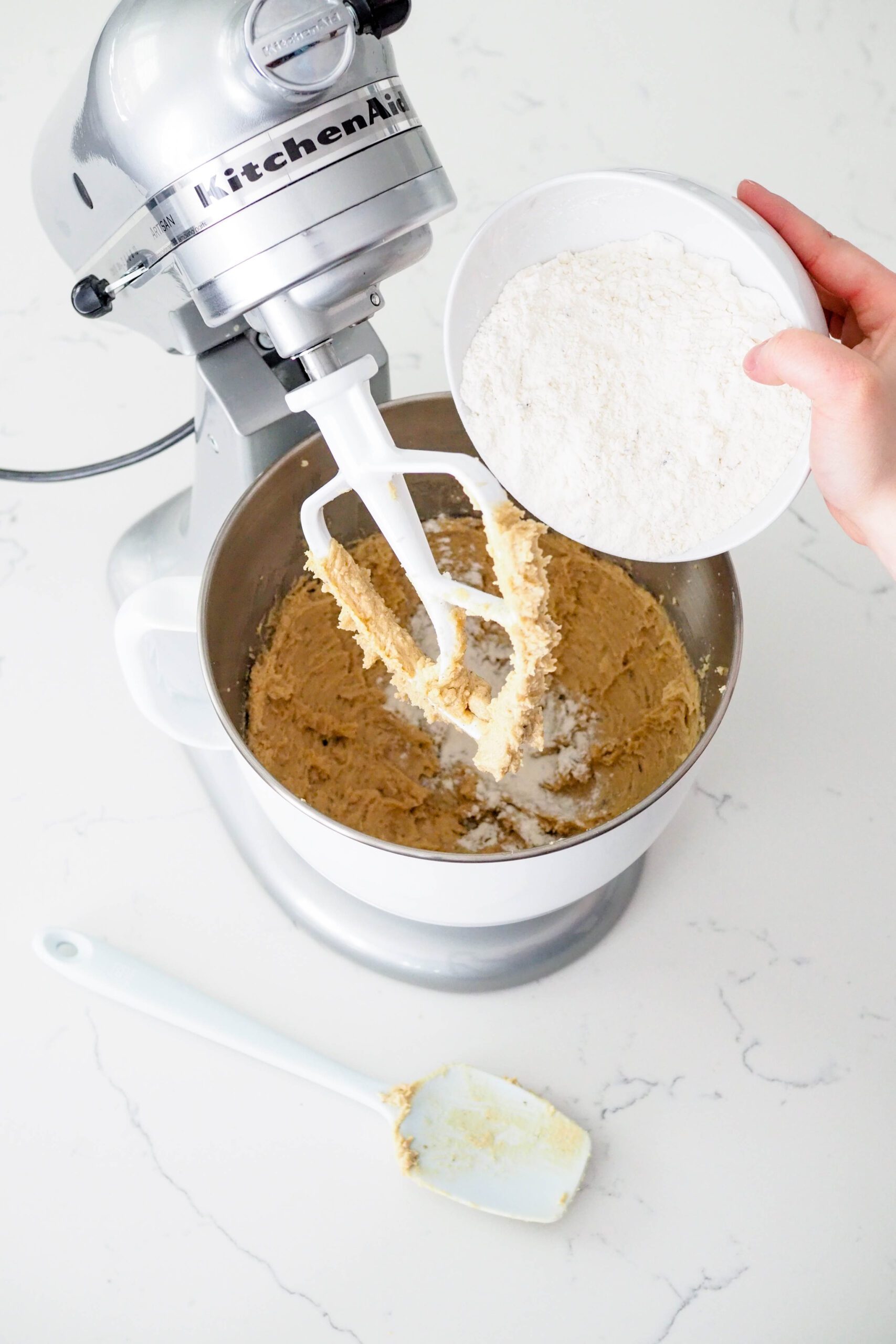 A bowl of flour and lavender buds is dumped into the bowl of a stand mixer.